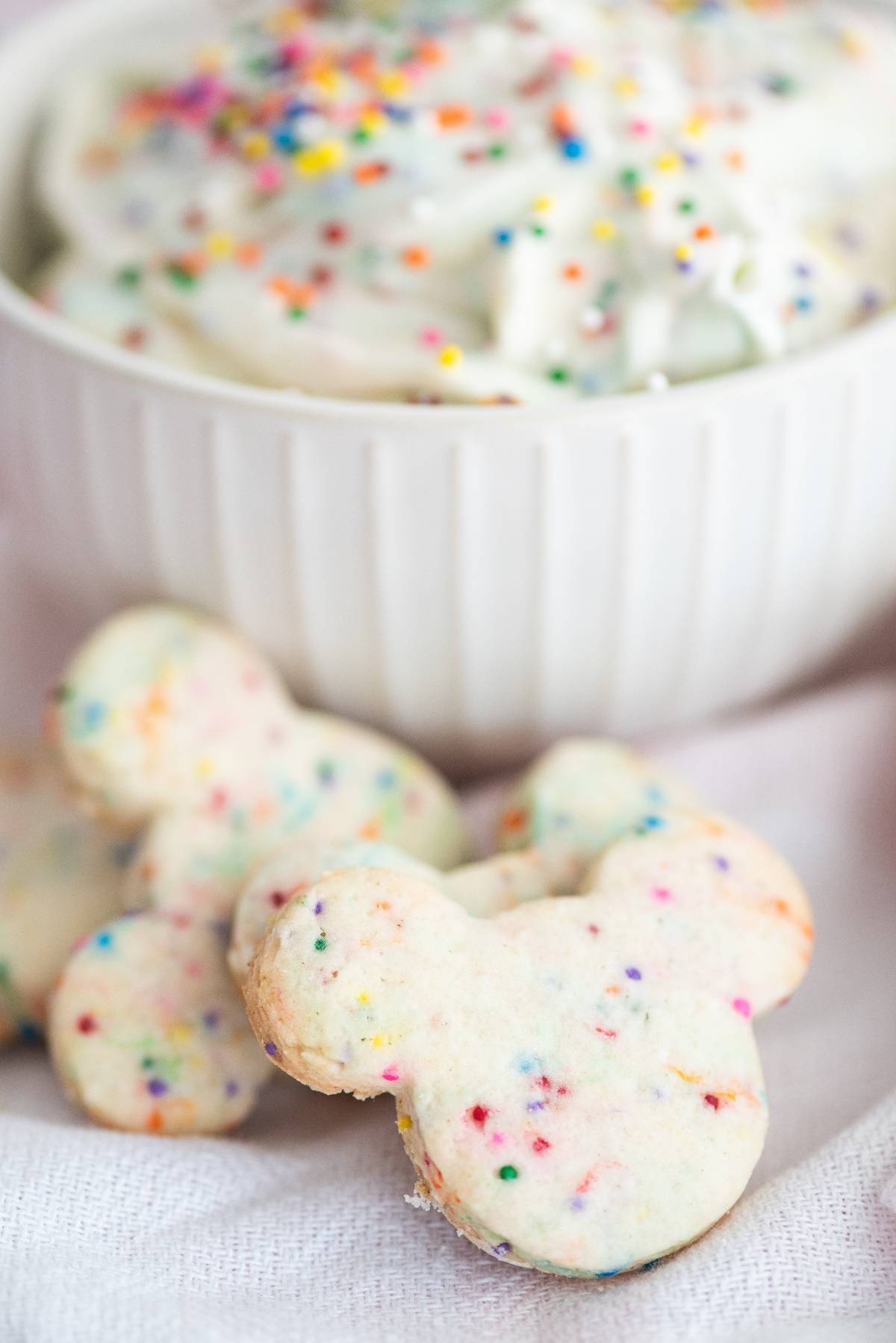 Mickey-shaped rainbow sprinkle cookies are paired with a bowl of cream cheese sprinkle dip in the background—perfect for Disney Sugar Cookies with Dip fans.