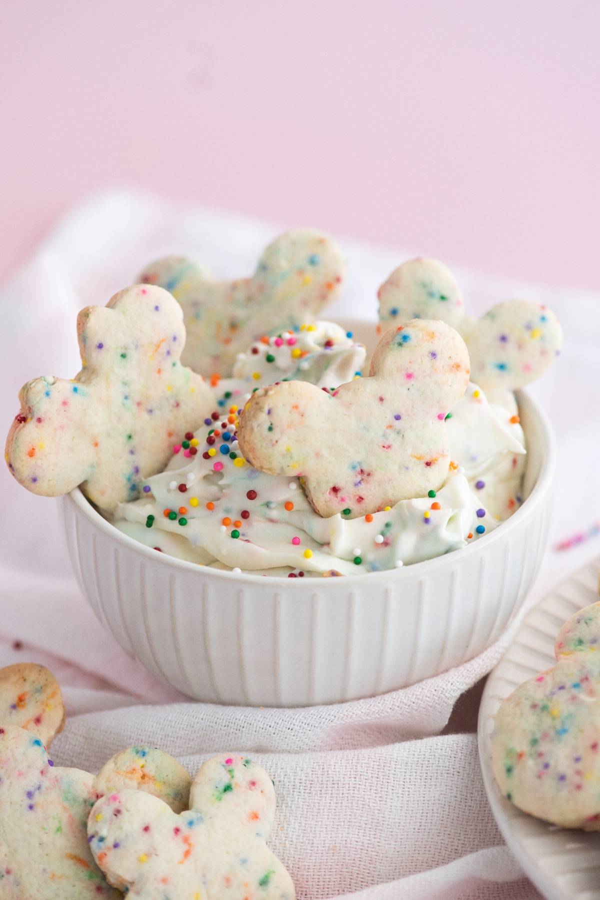Bowl of cream cheese sprinkle dip topped with rainbow sprinkles and Disney Sugar Cookies with Dip, including Mickey-shaped funfetti cookies.