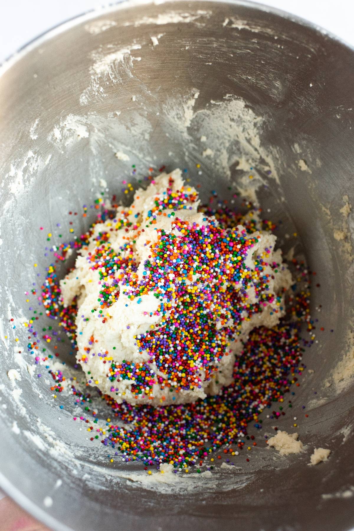 Cookie dough in a metal bowl topped with colorful round sprinkles, just like classic Funfetti Dunkaroo dip, ready to be mixed.