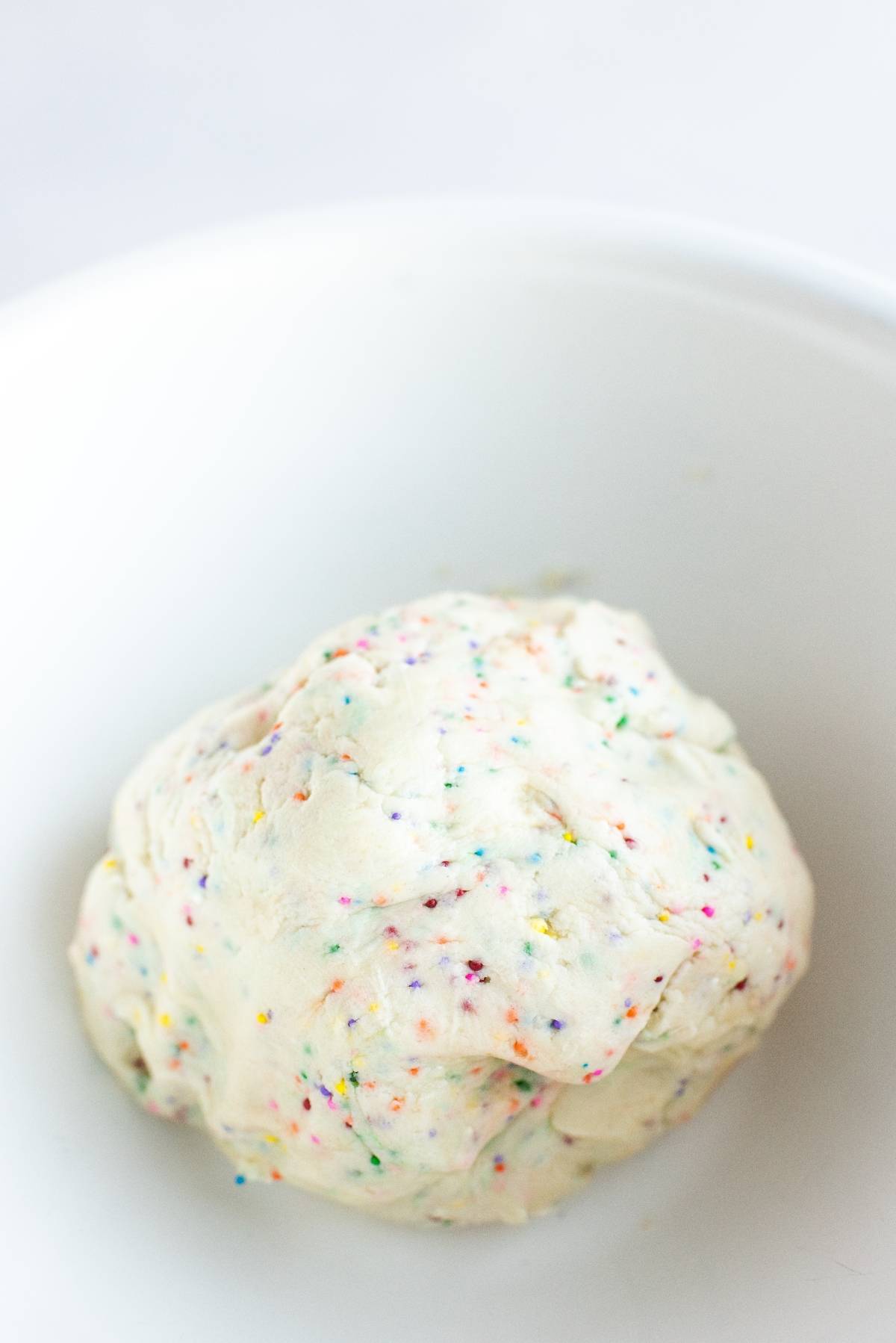 A ball of white cookie dough with colorful sprinkles in a white bowl, perfect for making Disney Sugar Cookies with Dip.