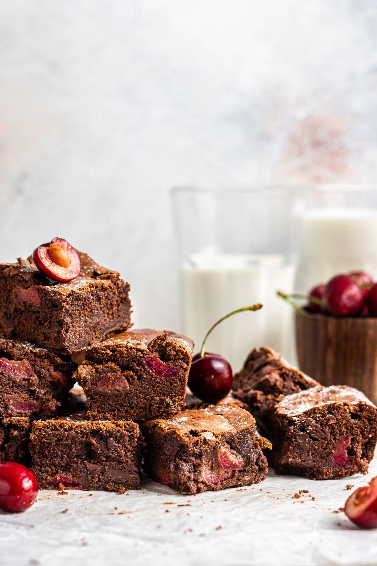 Stacked Double Chocolate Cherry Brownies with fresh cherries, set against a backdrop of glasses of milk.
