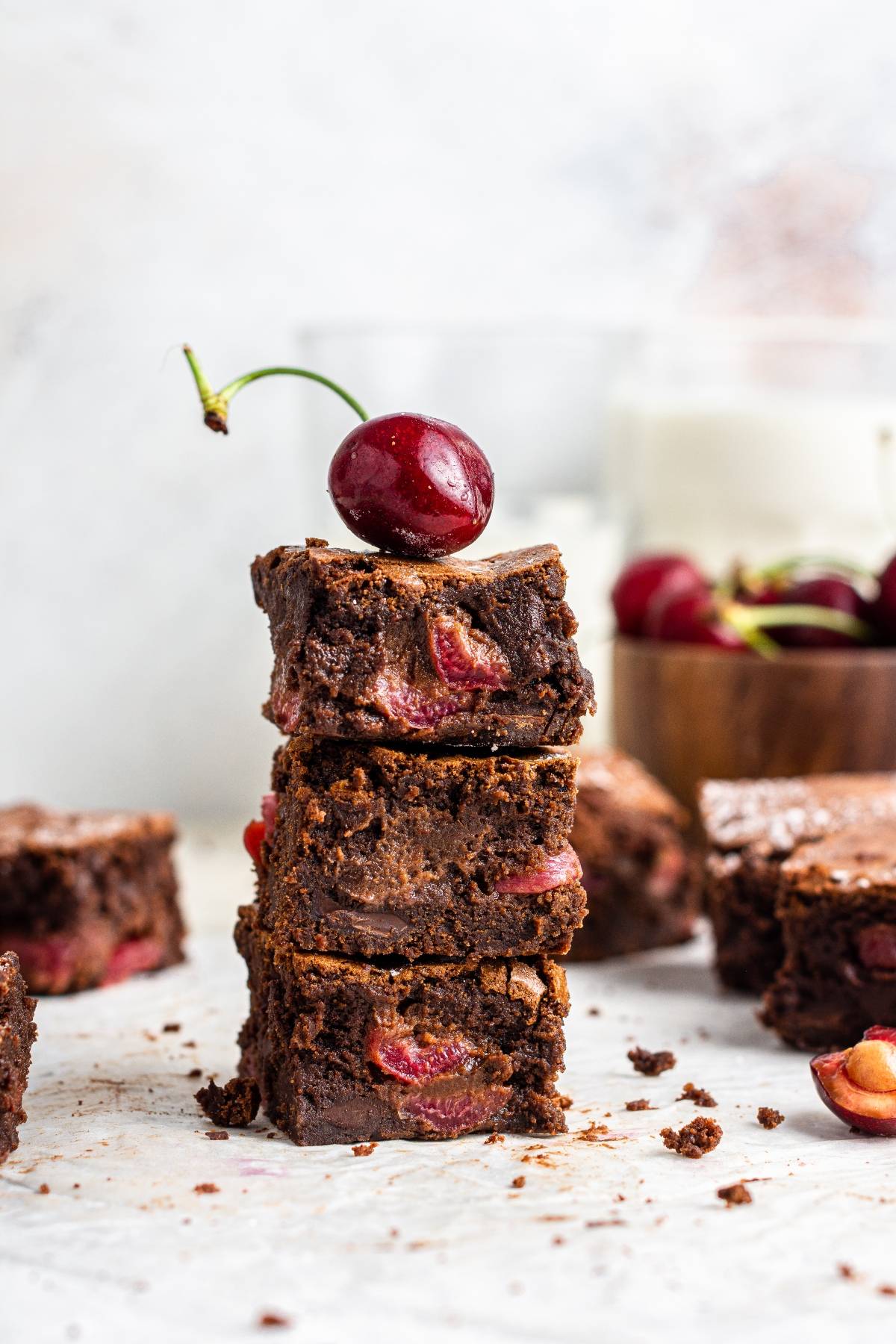 Stack of three fresh cherry brownies with a whole cherry on top; more brownies and cherries in the background—an easy cherry dessert that’s rich, fudgy, and perfect for any occasion.
