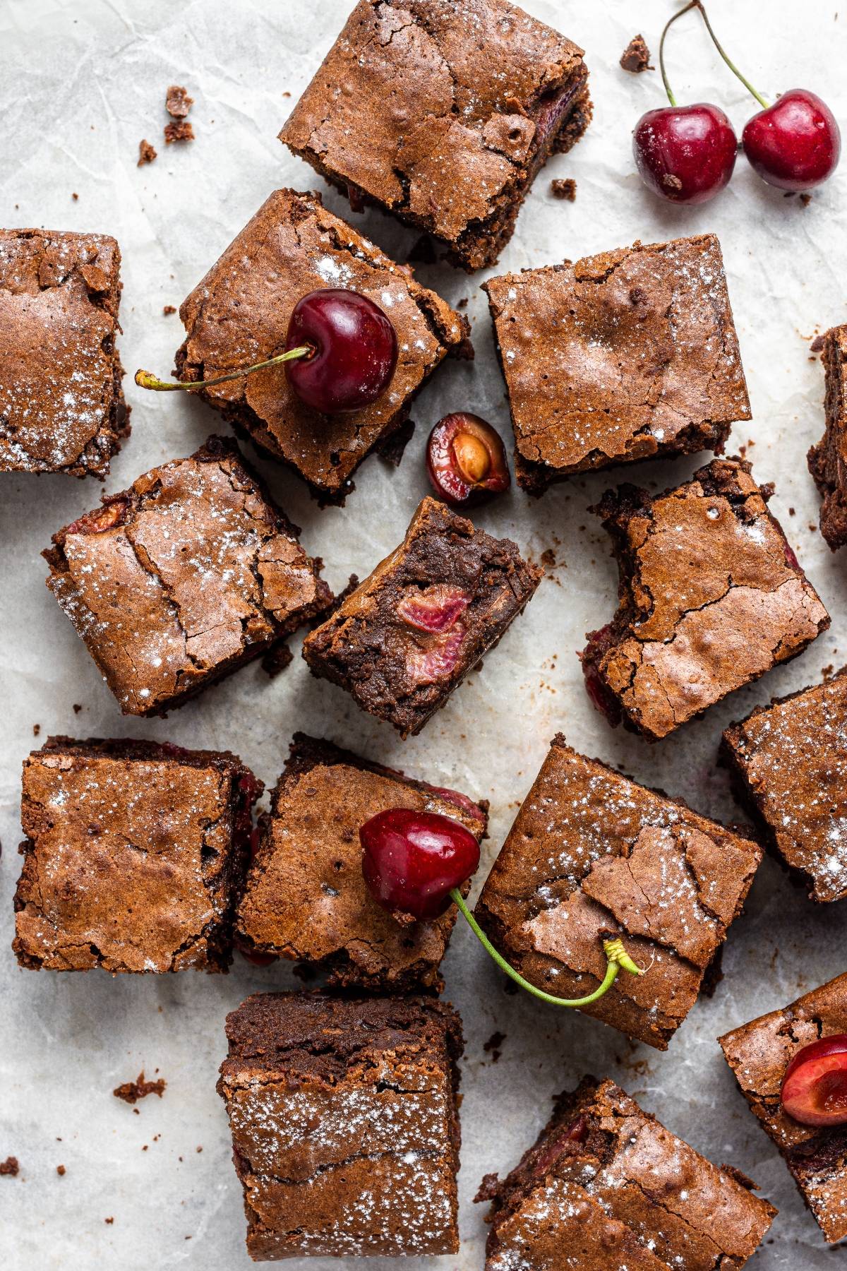 Fudgy Double Chocolate Cherry Brownies with fresh cherries, some whole and some bitten, arranged on a light background—a delicious chocolate and cherry dessert.