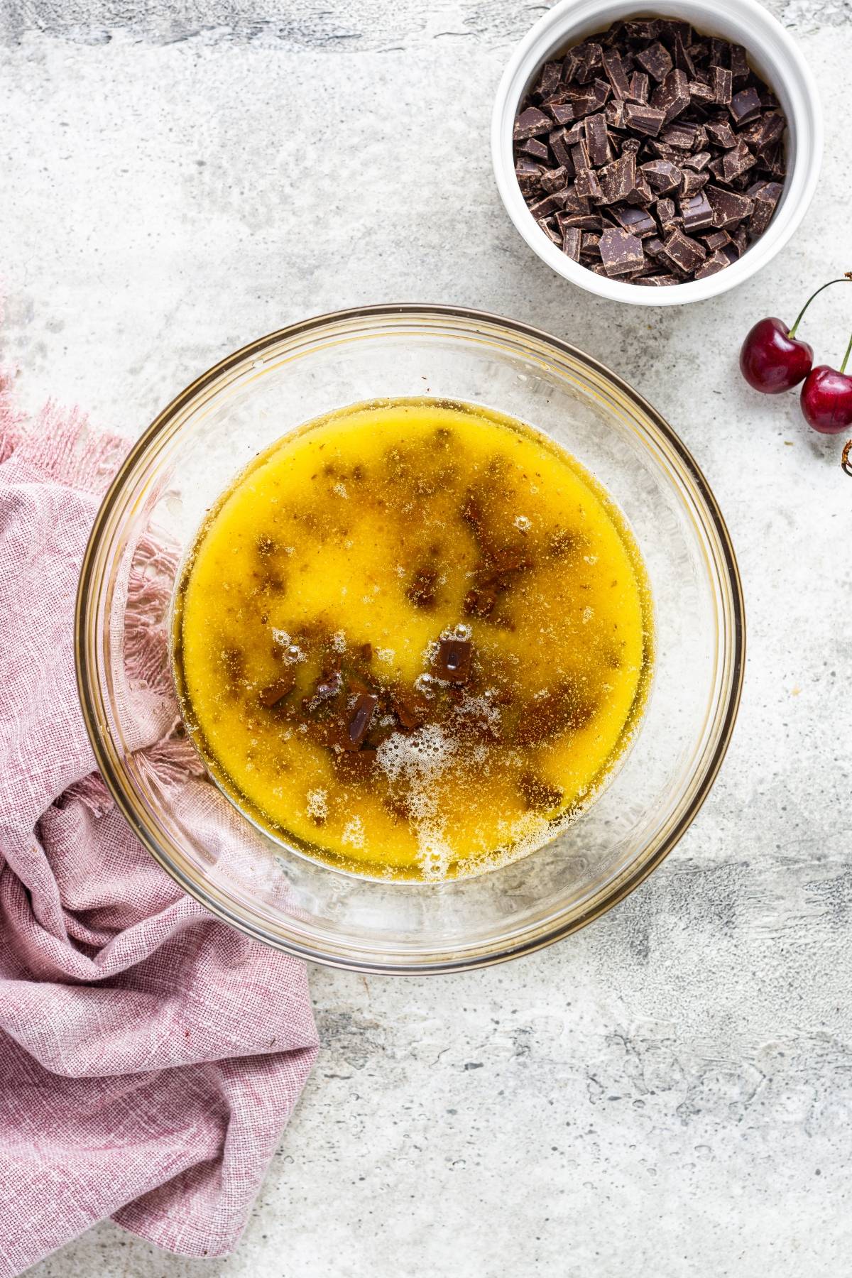 A glass bowl of melted butter and sugar sits beside chopped chocolate and cherries, ready to become a delicious Double Chocolate Cherry Brownies—a perfect chocolate and cherry dessert.