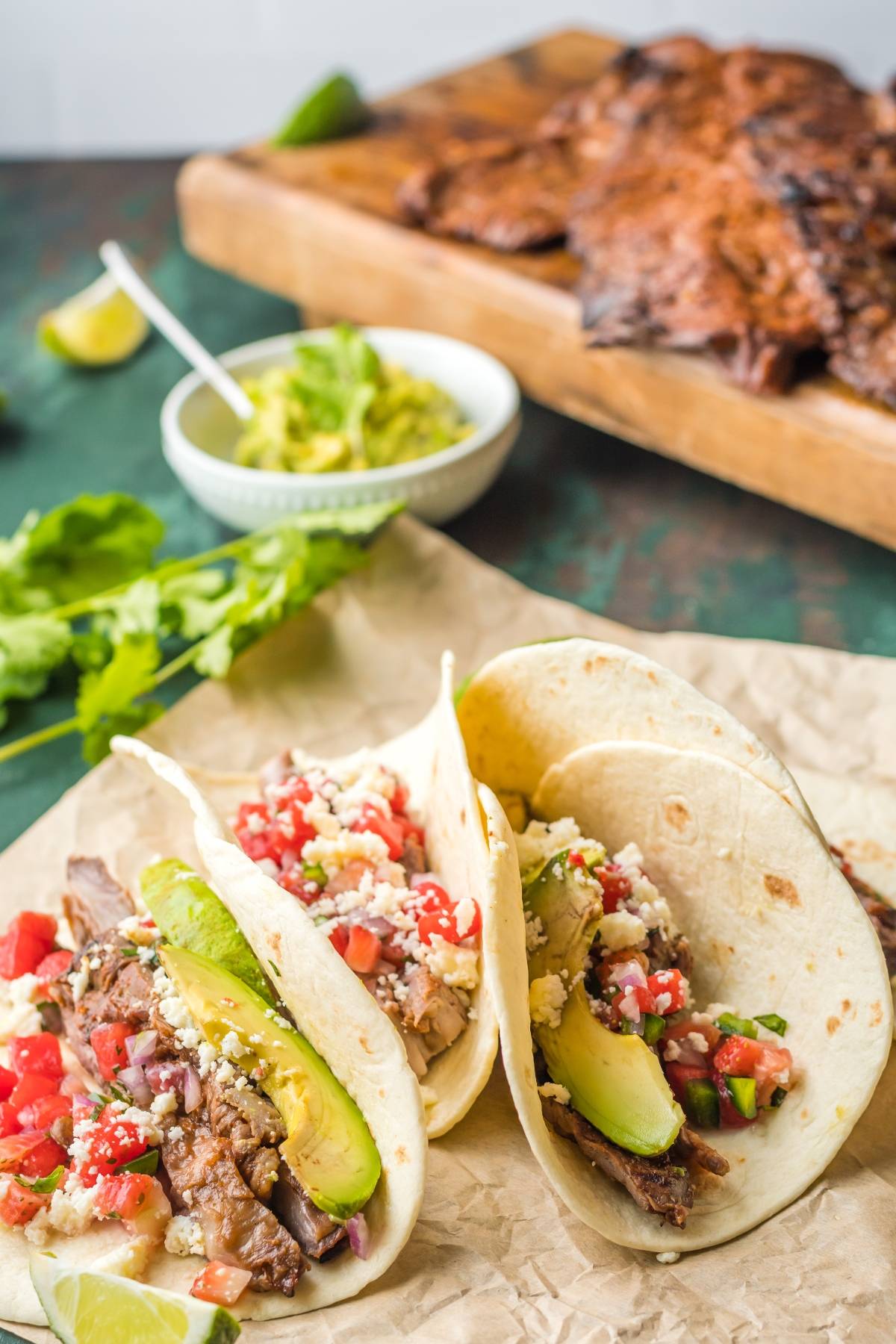 Two delicious flank steak tacos with avocado, pico de gallo, and cheese on tortillas, served with guacamole and extra steak—perfect for trying out your best flank steak marinade or favorite flank steak recipe.