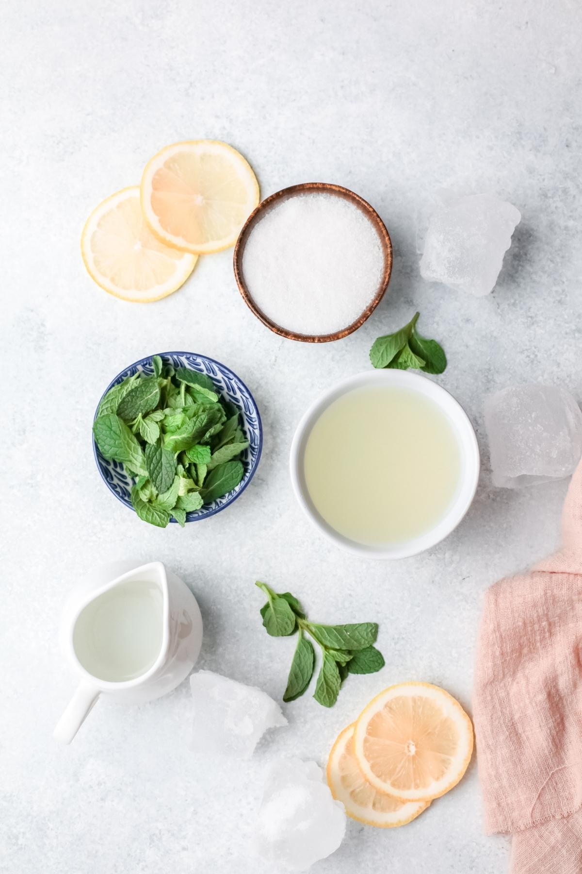 Lemon slices, mint leaves, sugar, lemon juice, and ice cubes arranged on a light surface—perfect ingredients for a refreshing Limonana or classic lemon and mint drink.