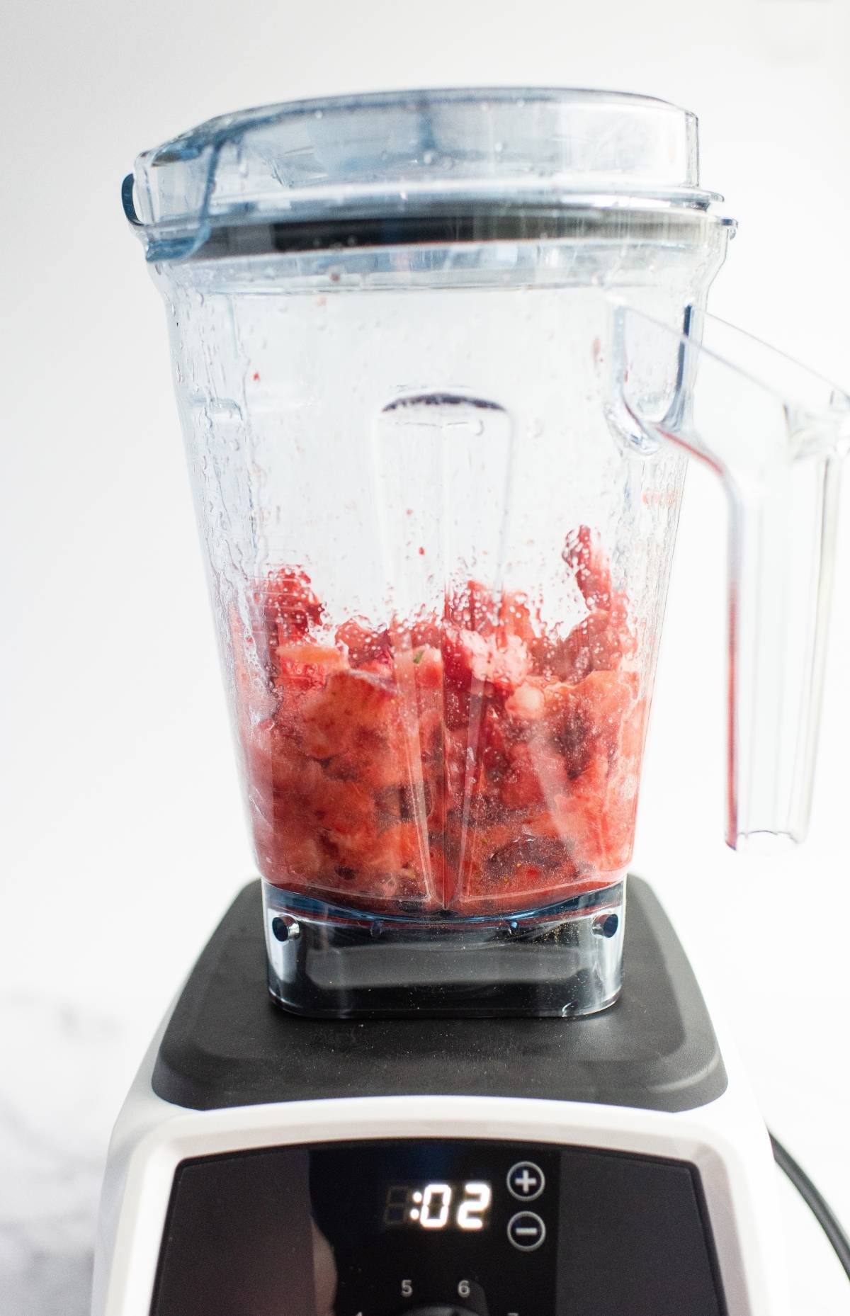 A blender partially filled with chopped strawberries, set to blend on a digital timer displaying 02 seconds—an easy way to make a daiquiri or enhance your favorite rum cocktail recipe.