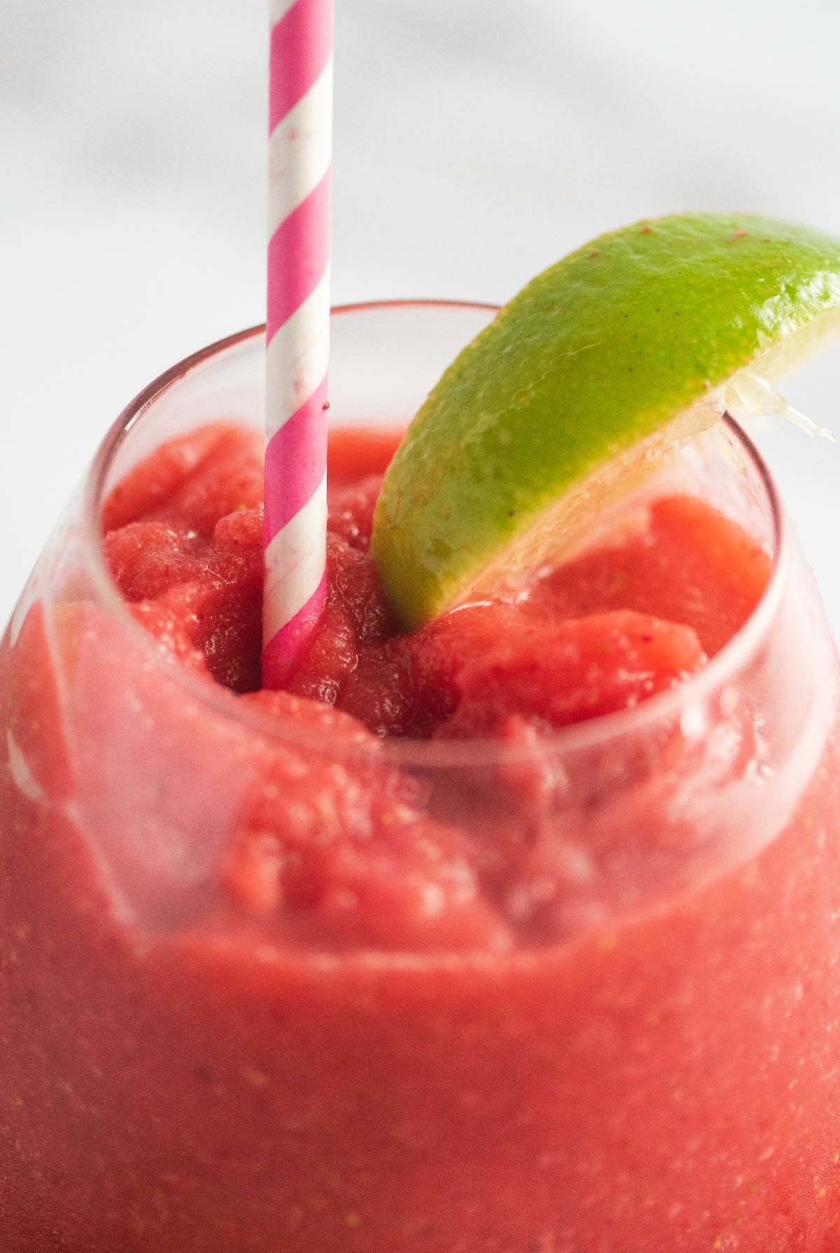 A glass of frozen strawberry lime daiquiri with a pink striped straw and a lime wedge on the rim—an easy way to make a daiquiri that's both refreshing and delicious.