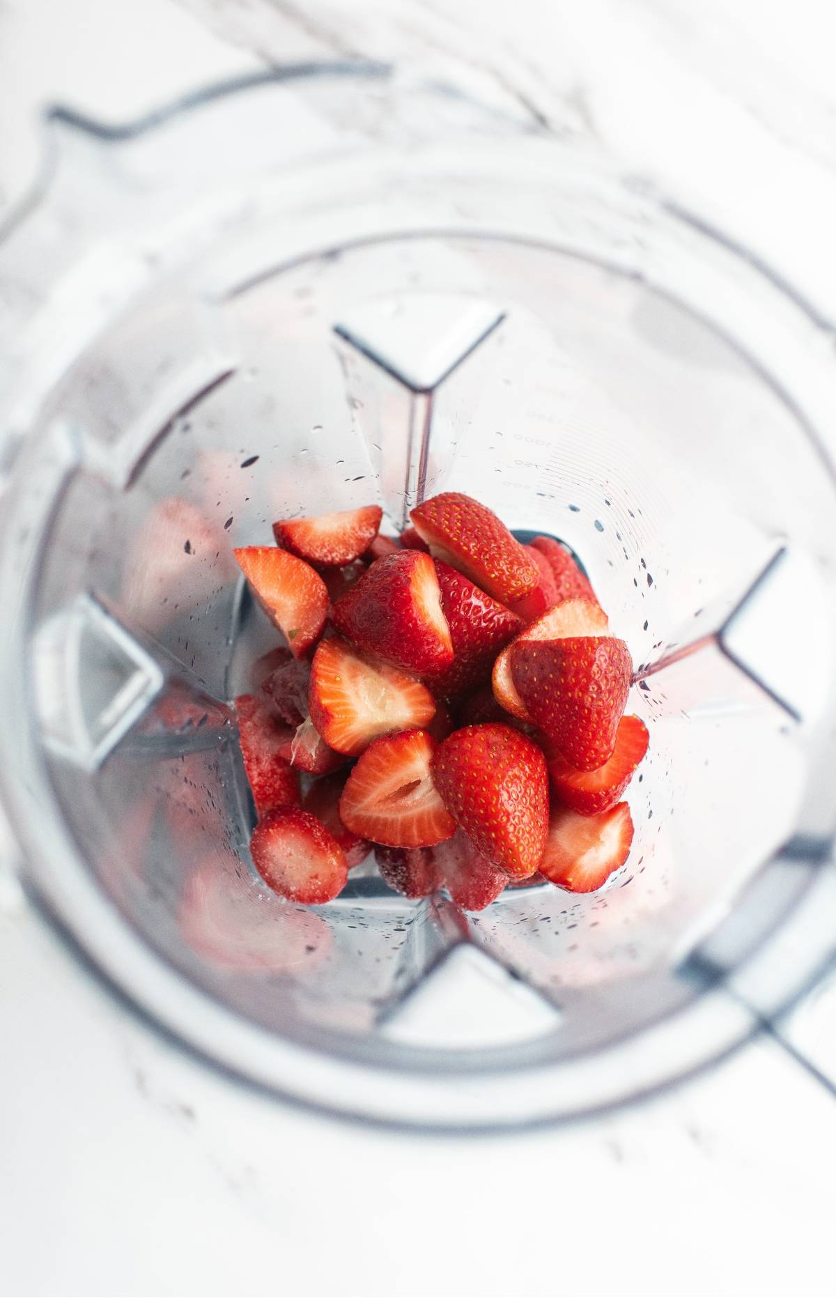 Halved strawberries inside a clear blender jar, viewed from above on a white surface—perfect for crafting the best daiquiri recipe or a refreshing frozen strawberry lime daiquiri.