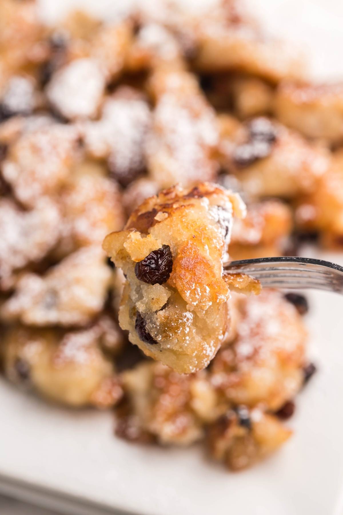 A fork holds a bite of golden, raisin-studded scrambled pancake, dusted with powdered sugar—a tempting taste of gluten free dessert pancake perfection.