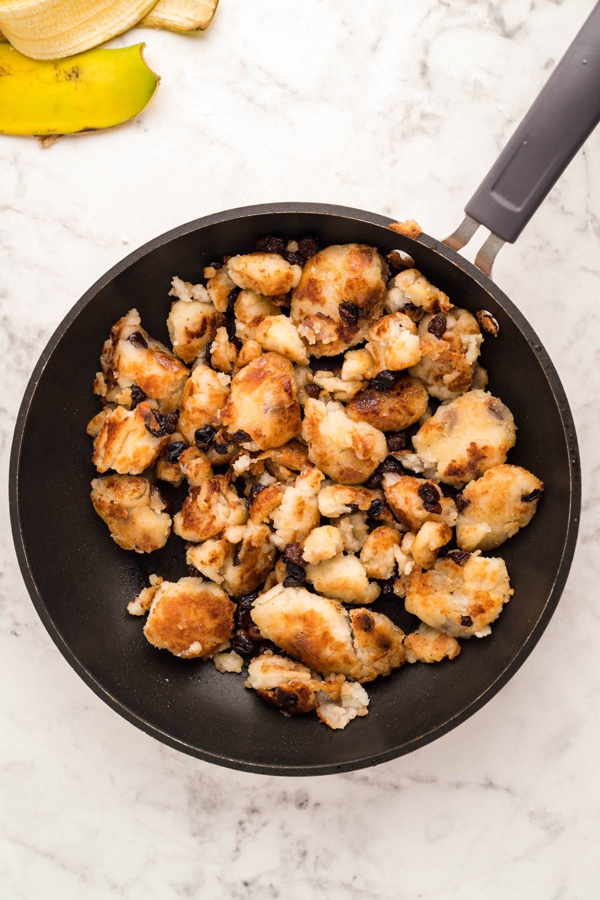 A black frying pan with browned, chunky Gluten Free Kaiserschmarrn pancakes and raisins sits on a marble countertop.