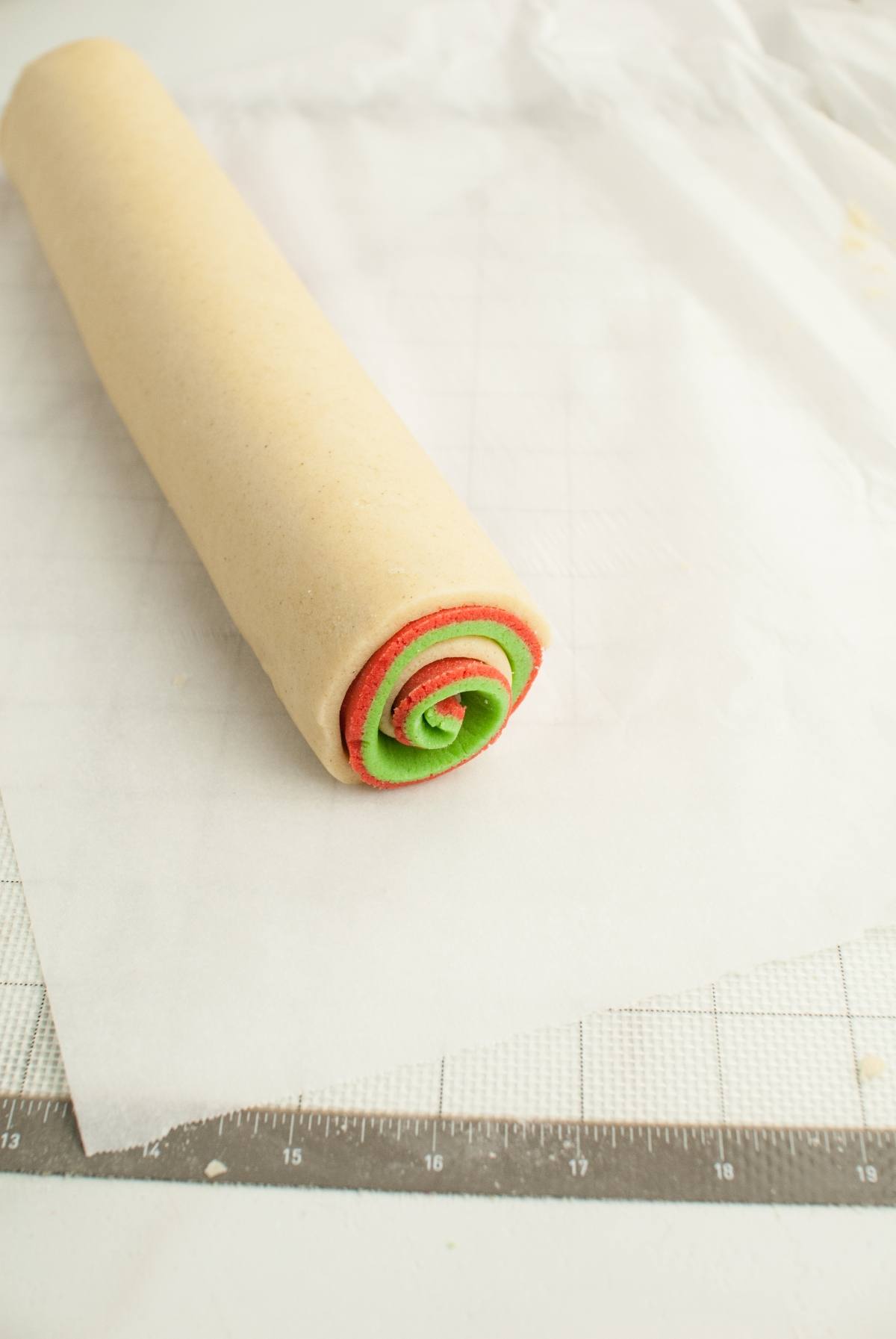 Rolled cookie dough log with a red and green spiral pattern on parchment paper atop a grid mat, perfect for making festive red and green Christmas cookies or Gluten Free Pinwheel Cookies.