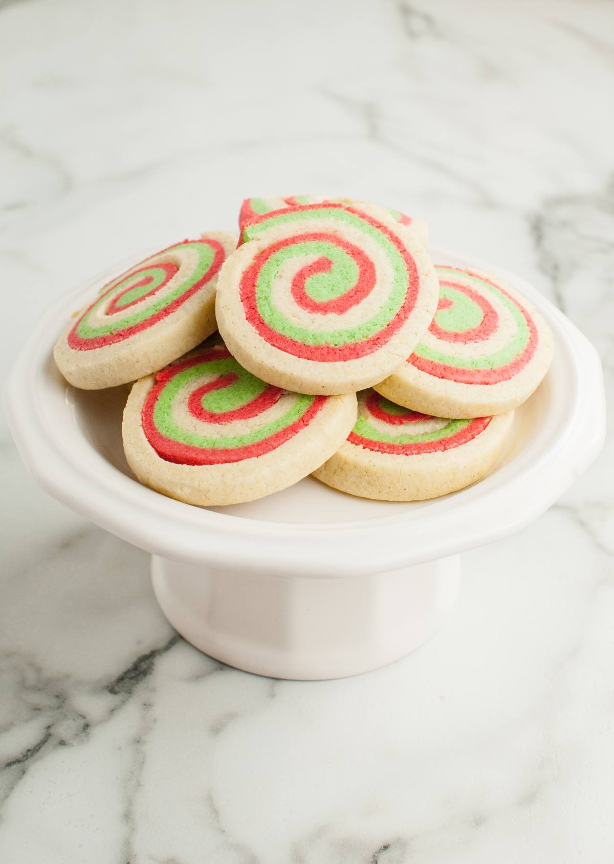 A plate of Italian Christmas swirl cookies with red and green spiral patterns on a white cake stand, perfect for gluten free holiday baking.