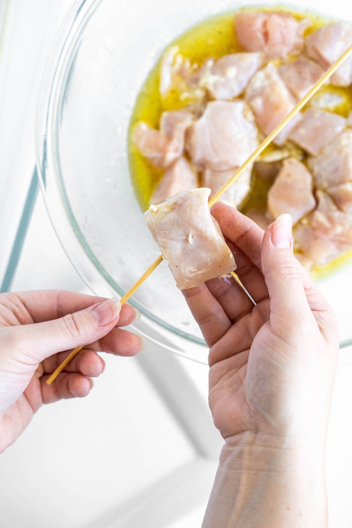 Hand skewering marinated raw chicken pieces for delicious grilled pepper and chicken kebabs over a glass bowl filled with more marinated chicken—perfect for your next summer BBQ dinner.