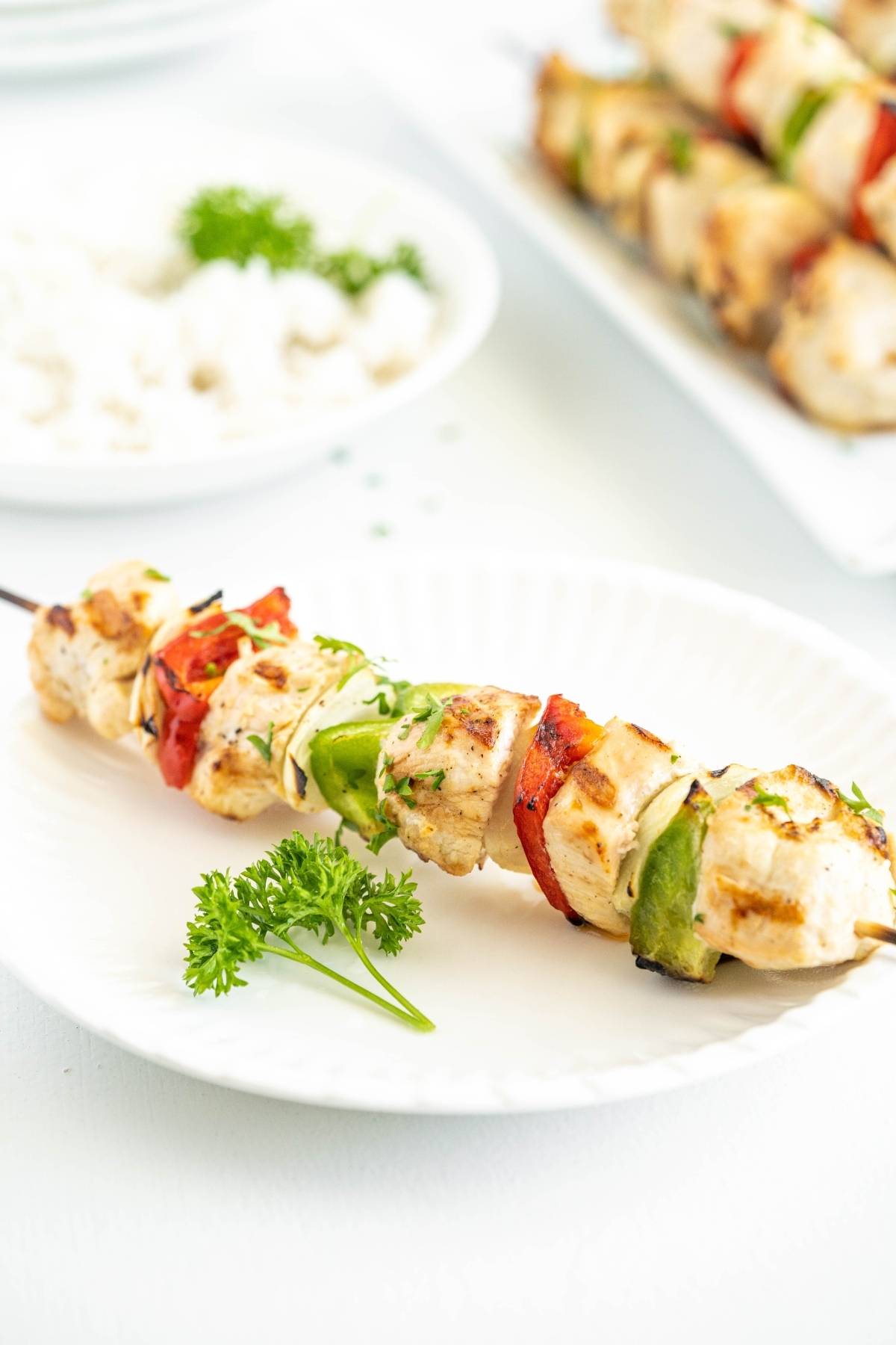 Tasty chicken skewers with red and green bell peppers on a white plate, garnished with parsley—perfect for a summer BBQ dinner.