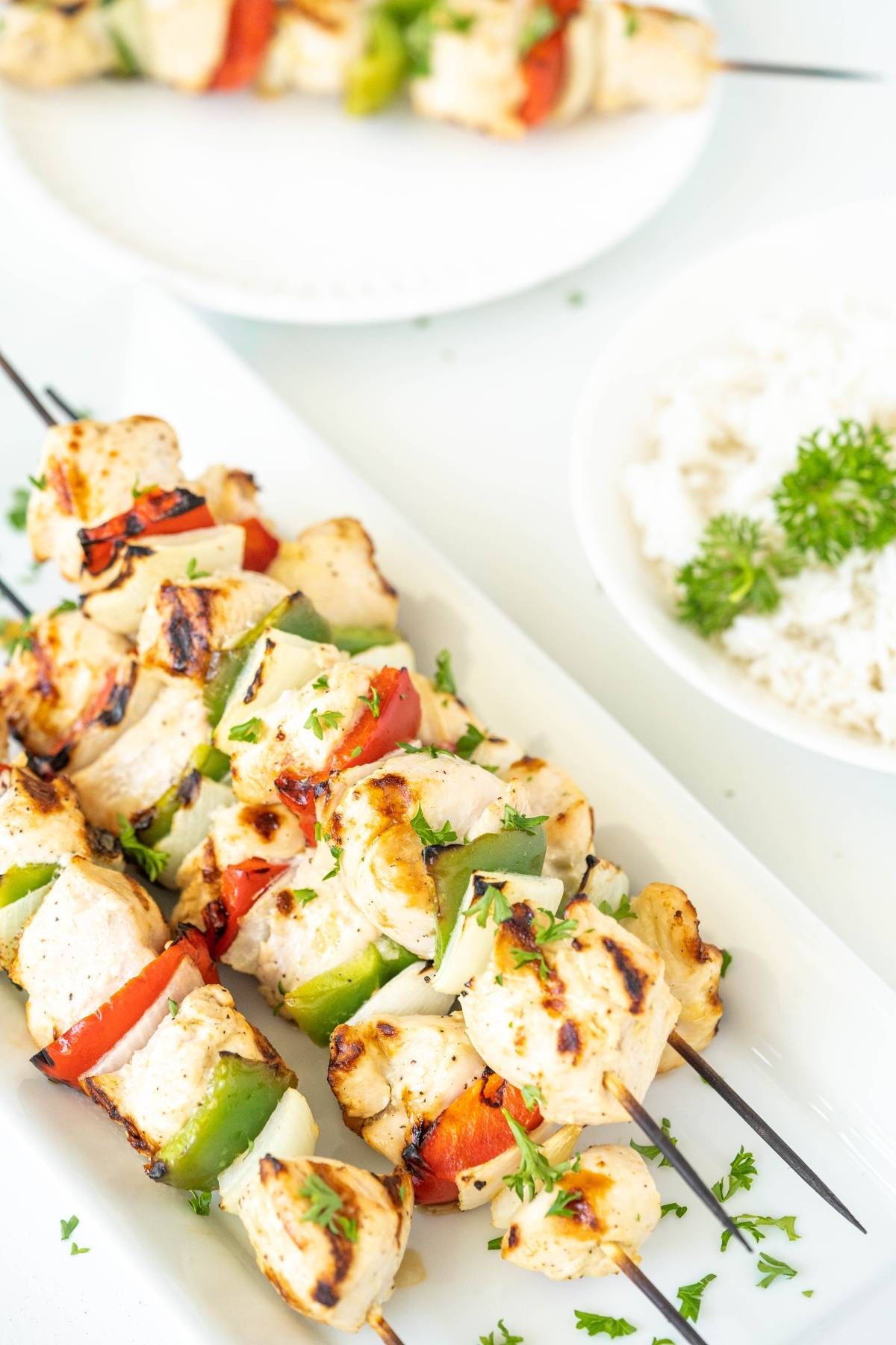 Grilled kebabs with chicken and vegetables—bell peppers and onions on skewers—served on a white plate with rice, perfect for a summer BBQ dinner.