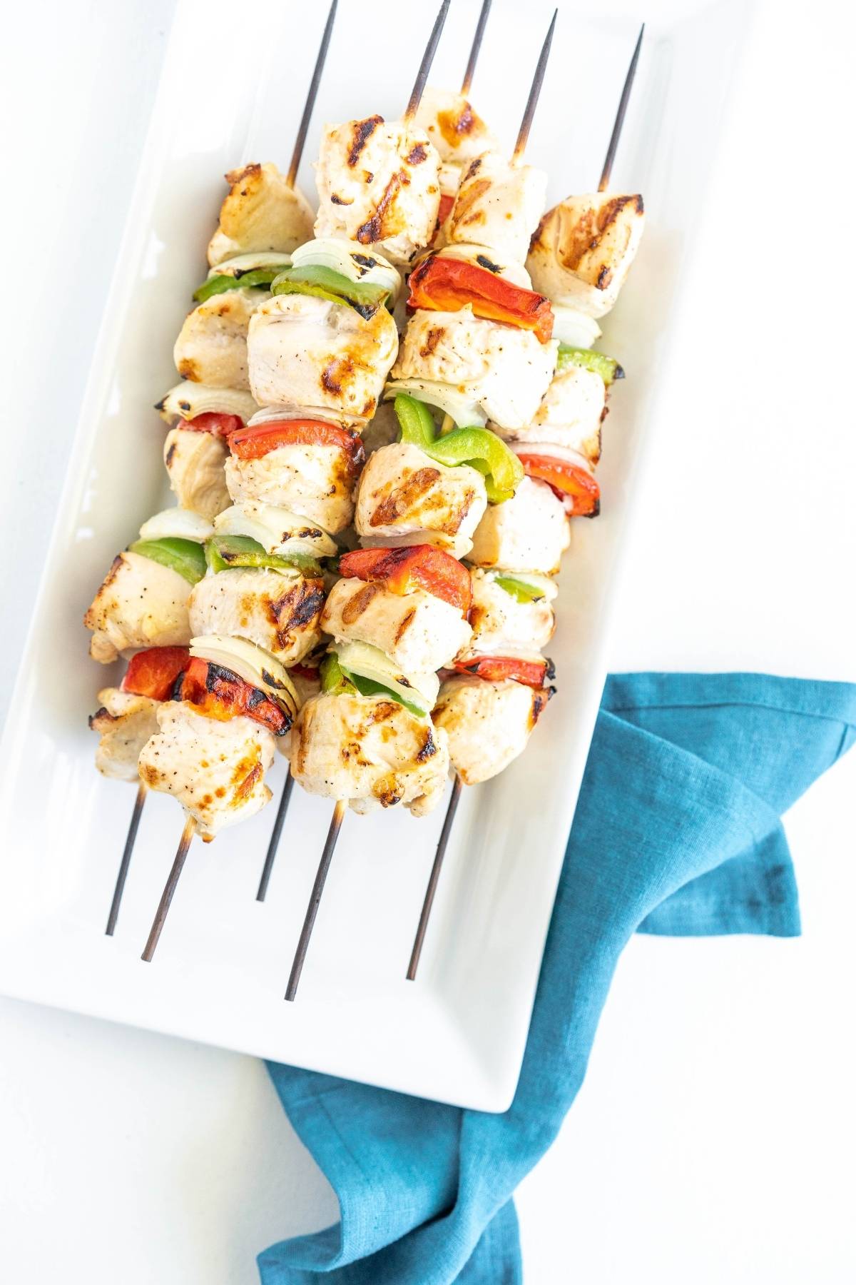 Grilled pepper and chicken kebabs are served on a white plate with a blue napkin underneath—perfect for your next summer BBQ dinner.