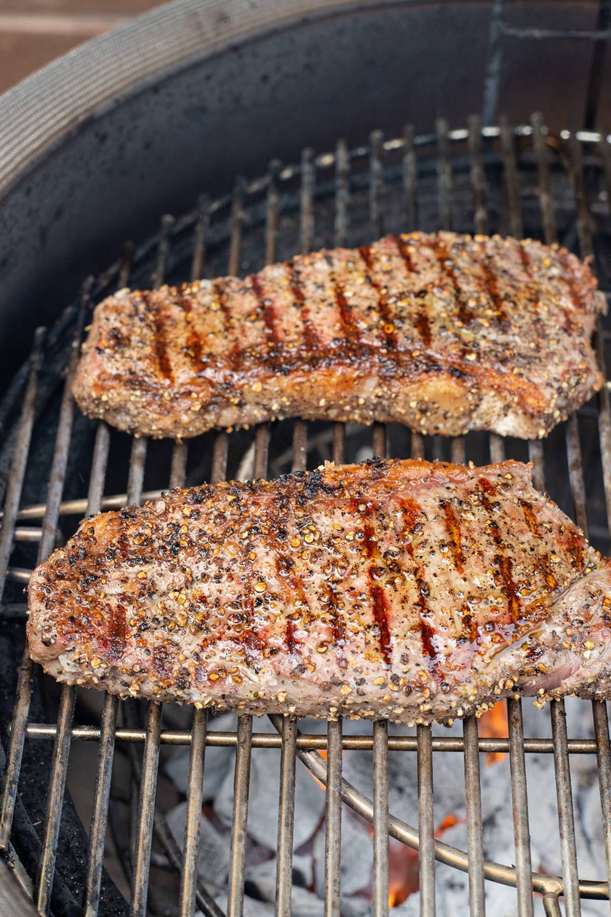 Two seasoned steaks with grill marks sizzle over open flames, perfect for a classic BBQ steak recipe.