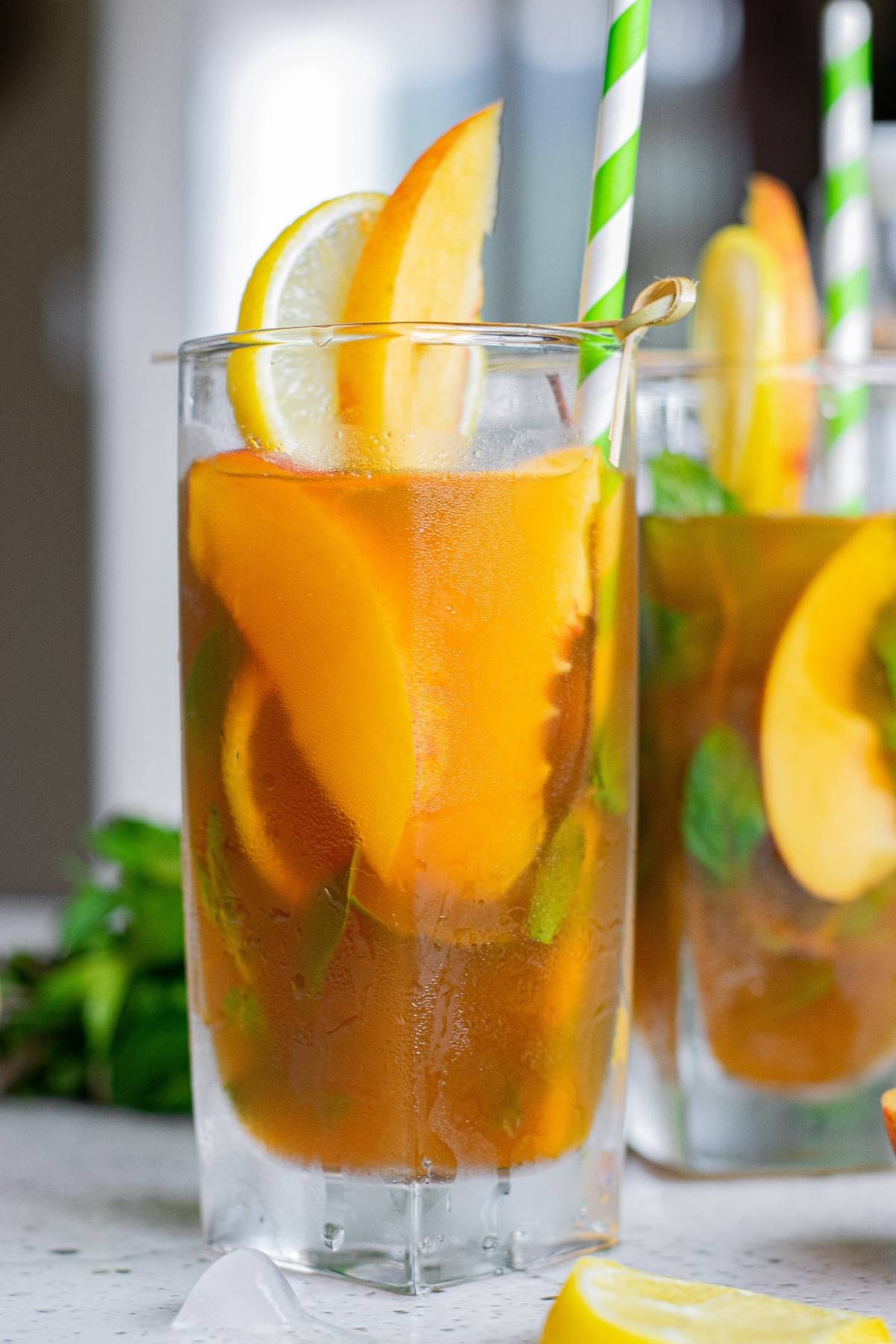 Iced tea with lemon and orange slices, mint leaves, and a green-striped straw in a glass—perfect for trying your own boozy iced tea recipe.