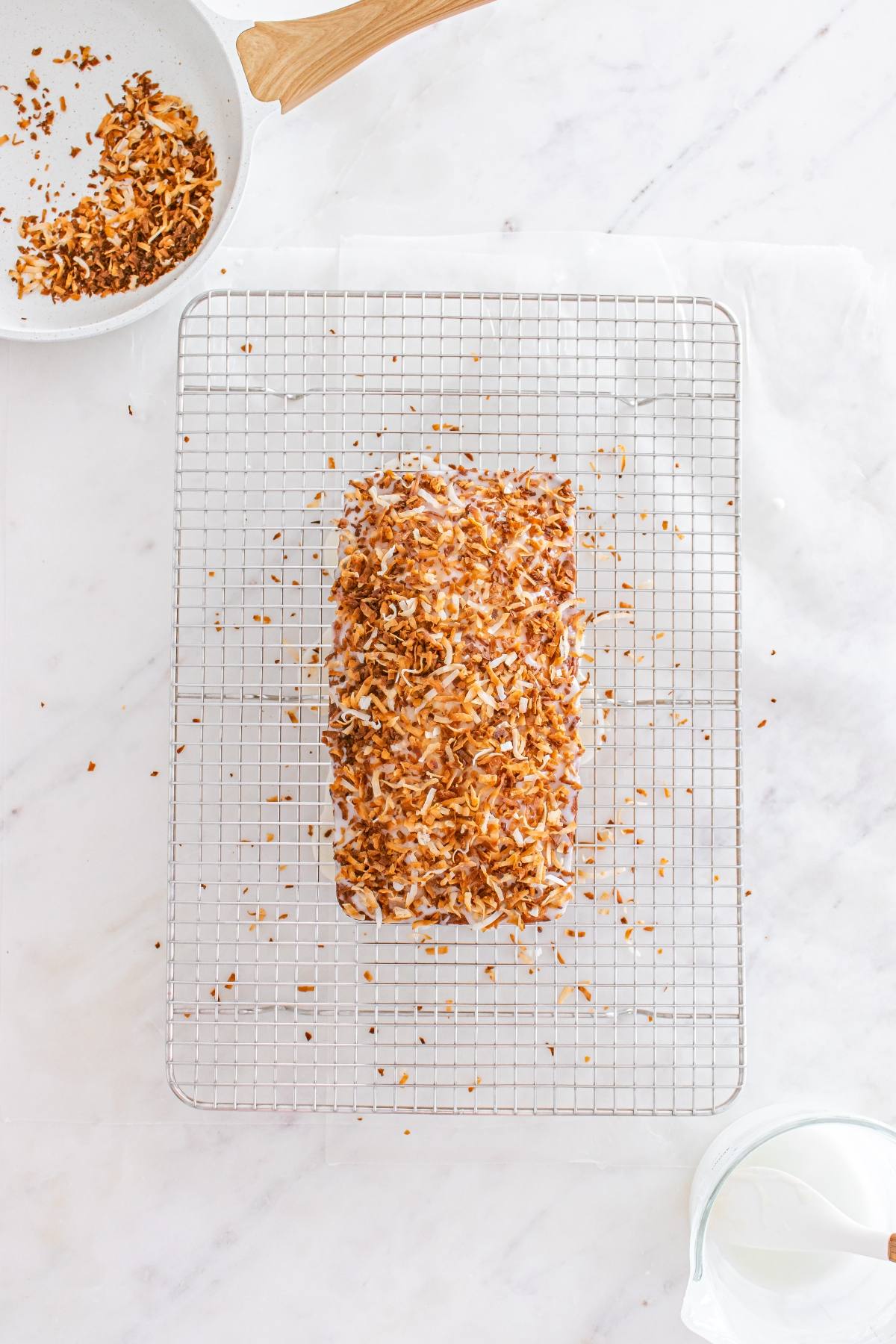 A loaf topped with toasted coconut sits on a wire rack over a marble surface.
