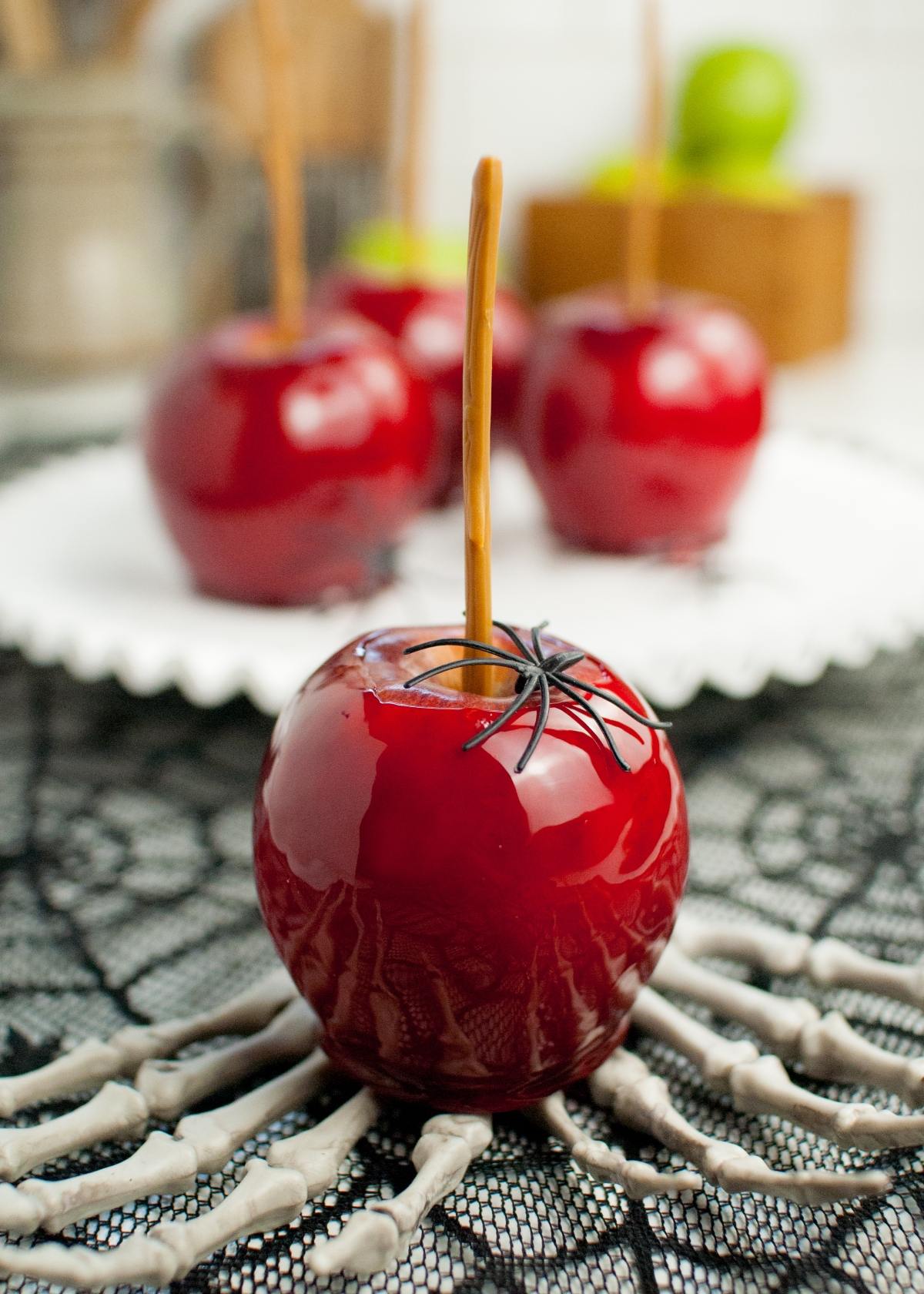 A shiny red candy apple with a fake spider, placed on a skeleton hand decoration, shows off the best candied apples—perfect for spooky parties or anyone wanting to learn how to make candy apples on a stick at home.