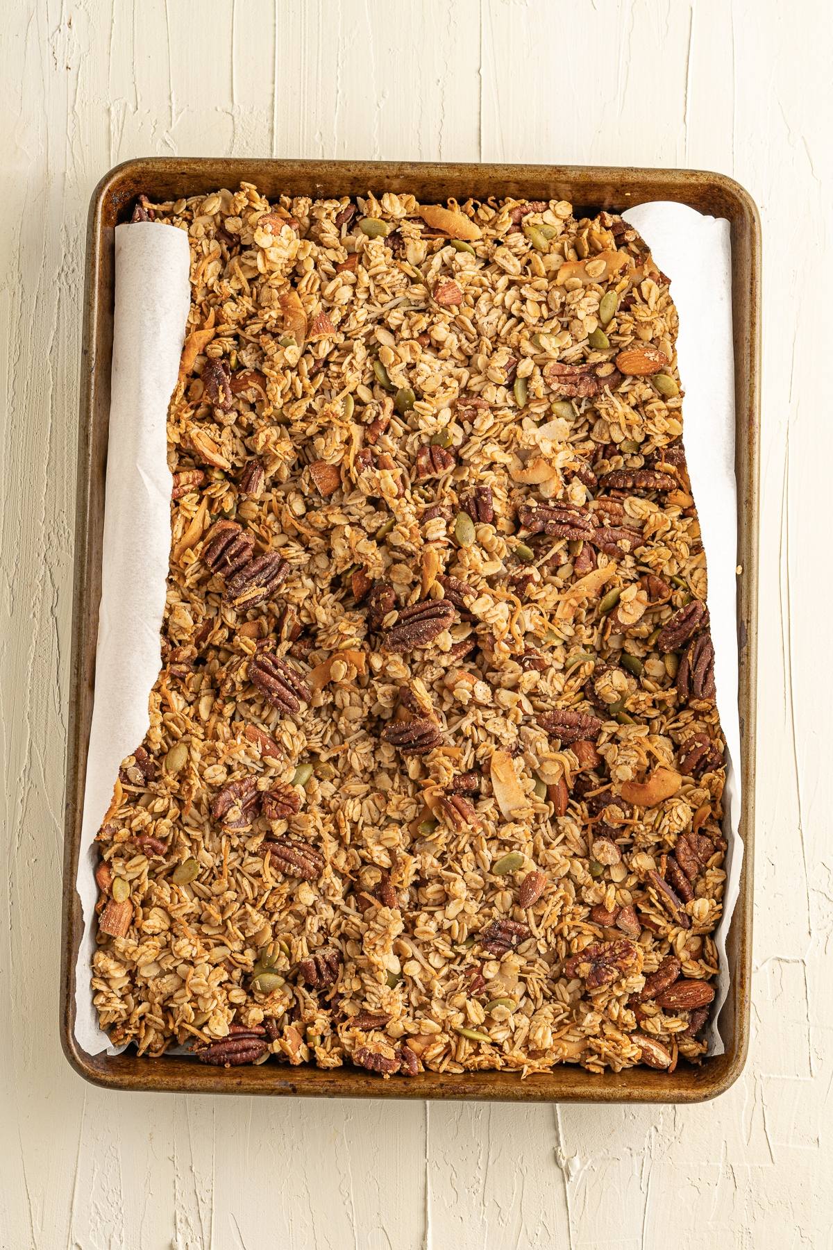 A baking tray lined with parchment paper filled with baked granola containing oats, nuts, and seeds—part of a healthy breakfast and perfect for those wanting the best gluten free granola.