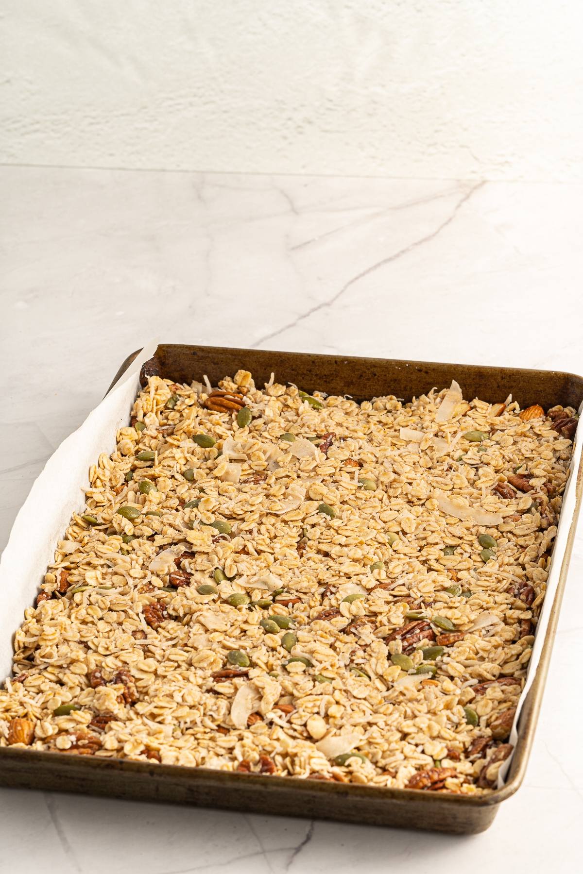 A baking tray with an even layer of easy homemade granola on a white marble surface.