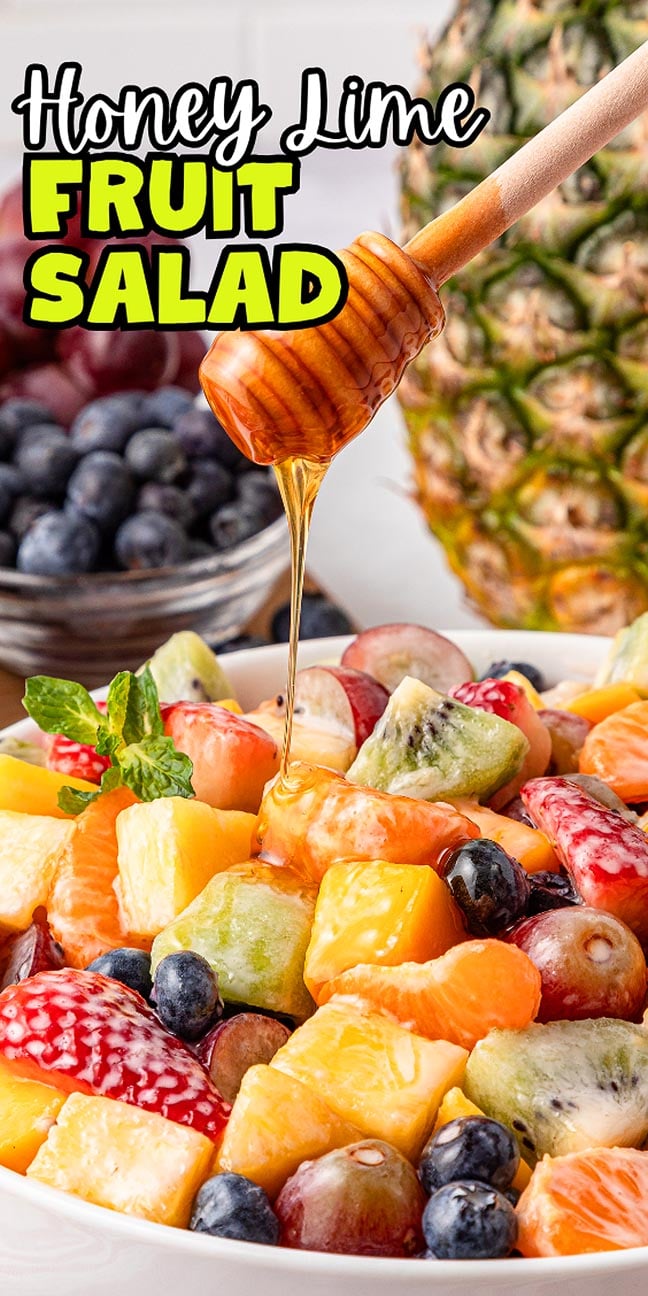 A honey dipper drizzles sweet honey over a vibrant honey lime fruit salad with strawberries, kiwi, and blueberries.