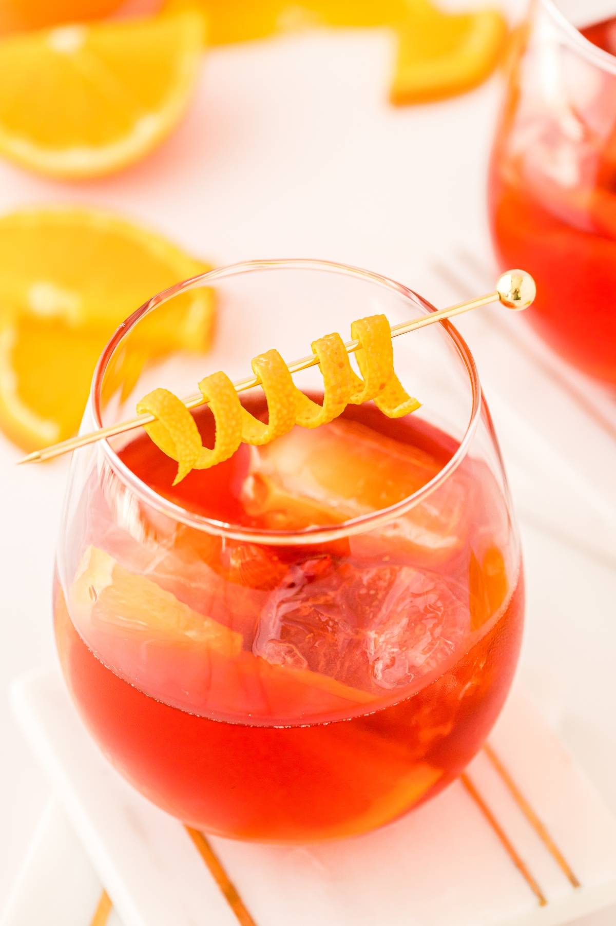 A glass of negroni cocktail with ice, garnished with an orange twist, sits next to orange slices—a classic Italian cocktail perfect for those wanting to know how to make the best negroni.