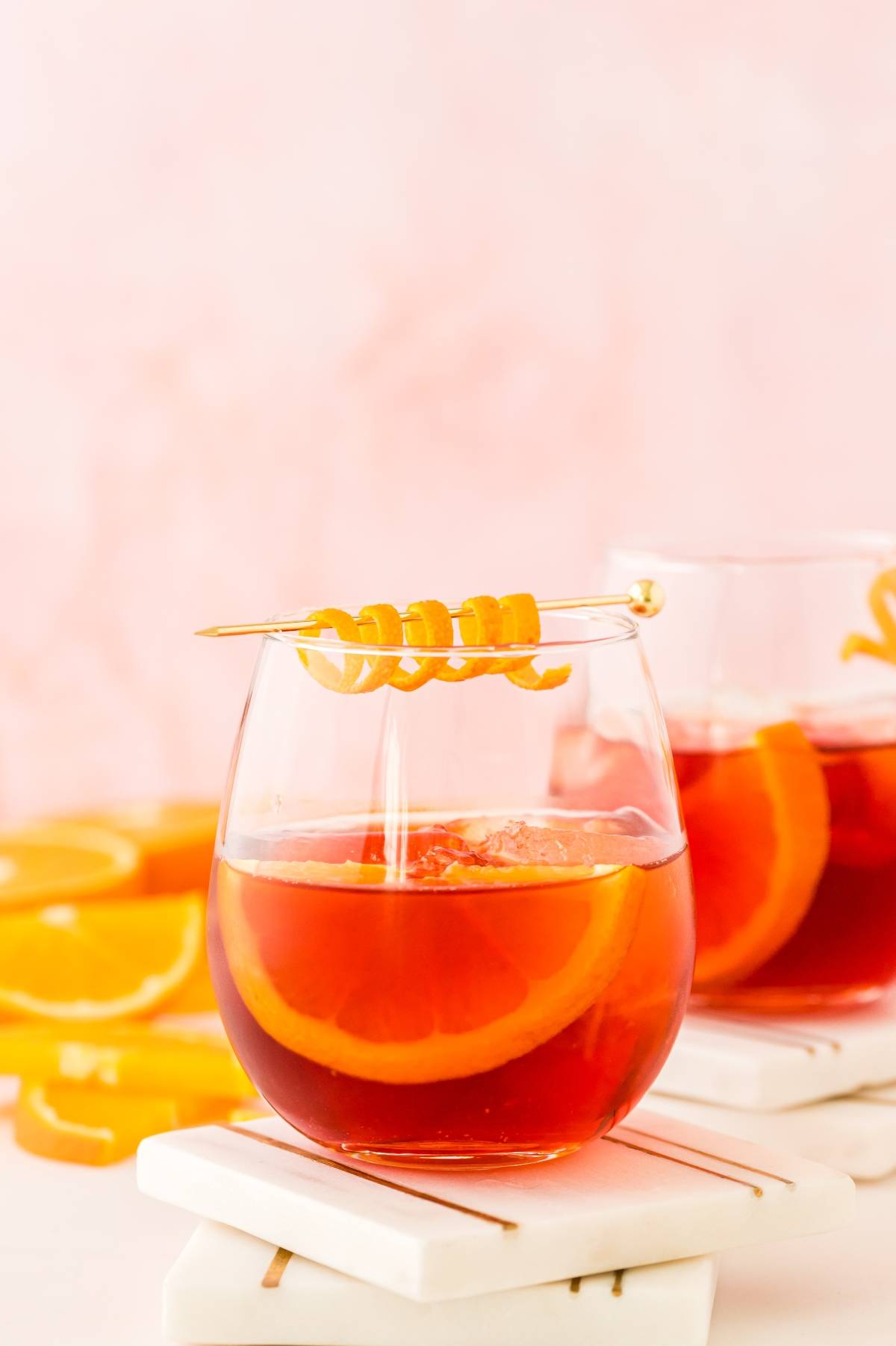 A glass of orange cocktail with ice, an orange slice, and a twisted peel garnish on a skewer—perfect for anyone curious about how to make the best negroni or seeking a vibrant cocktail with Campari.