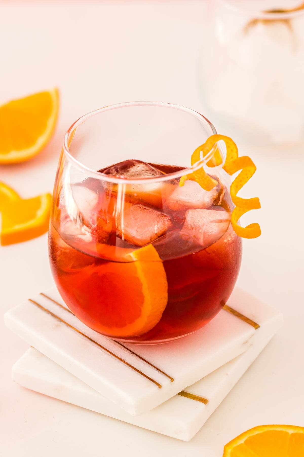 A glass of iced red cocktail with Campari, garnished with an orange slice and twist, sits on white coasters—a classic Italian cocktail presented in style.