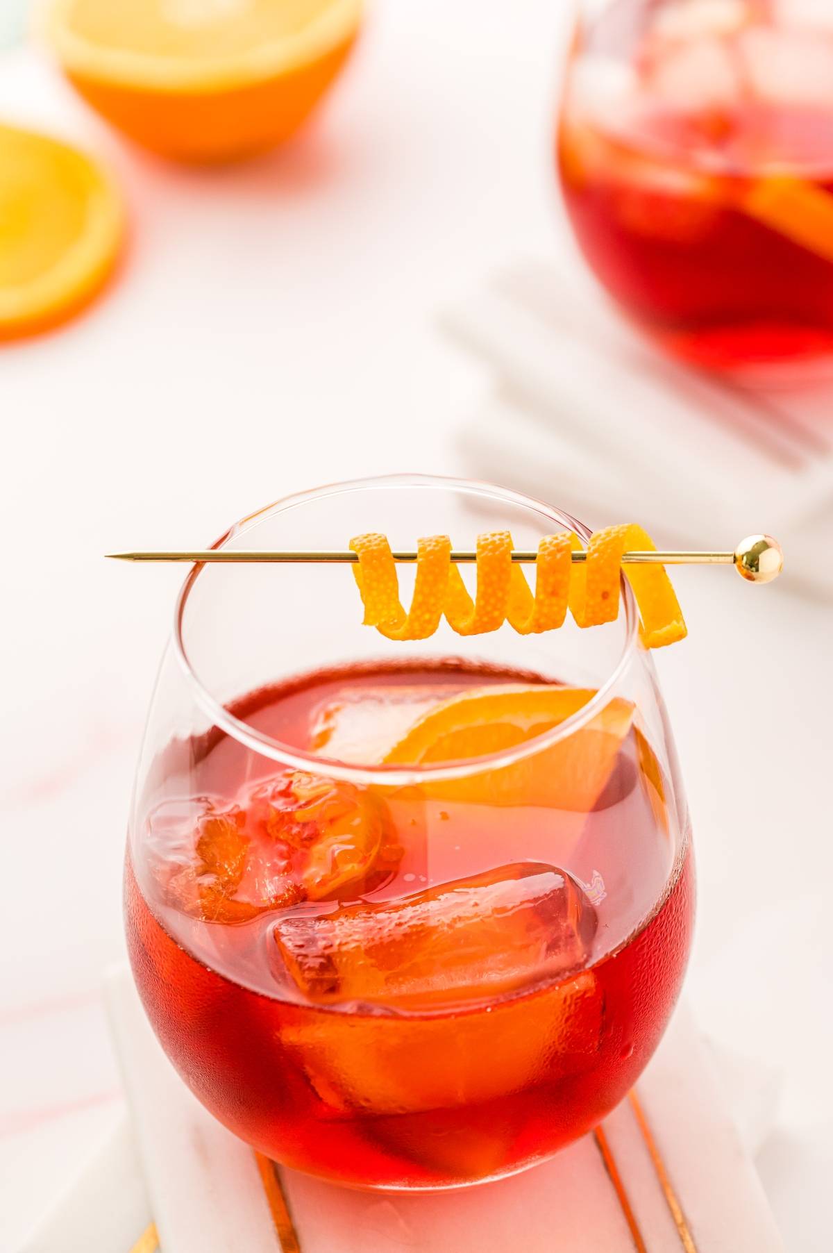 A glass of red cocktail with ice, orange slice, and orange twist garnish on a skewer—the perfect way to enjoy a classic Italian cocktail with Campari.