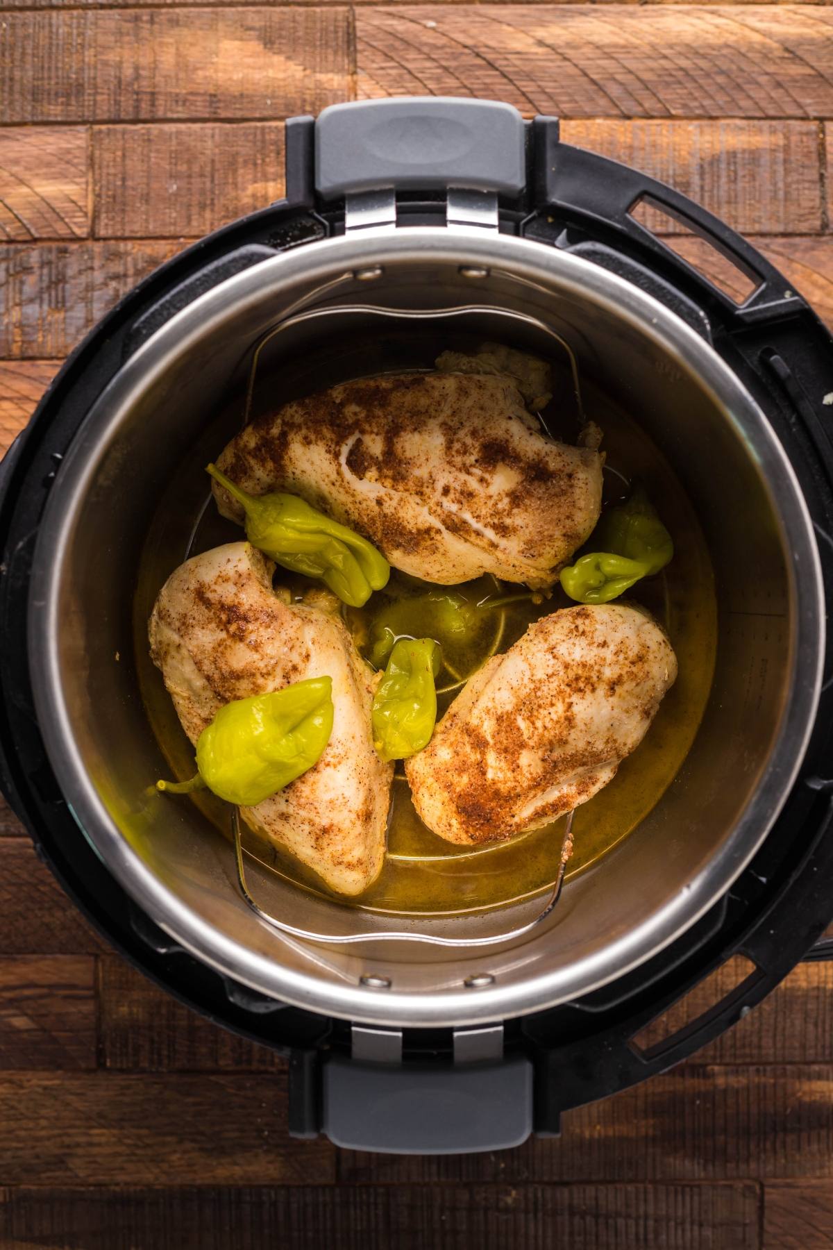 Three seasoned chicken breasts and pepperoncini peppers in an Instant Pot on a wooden surface, perfect for a flavourful Instant Pot dinner or quick 20 minute meal.
