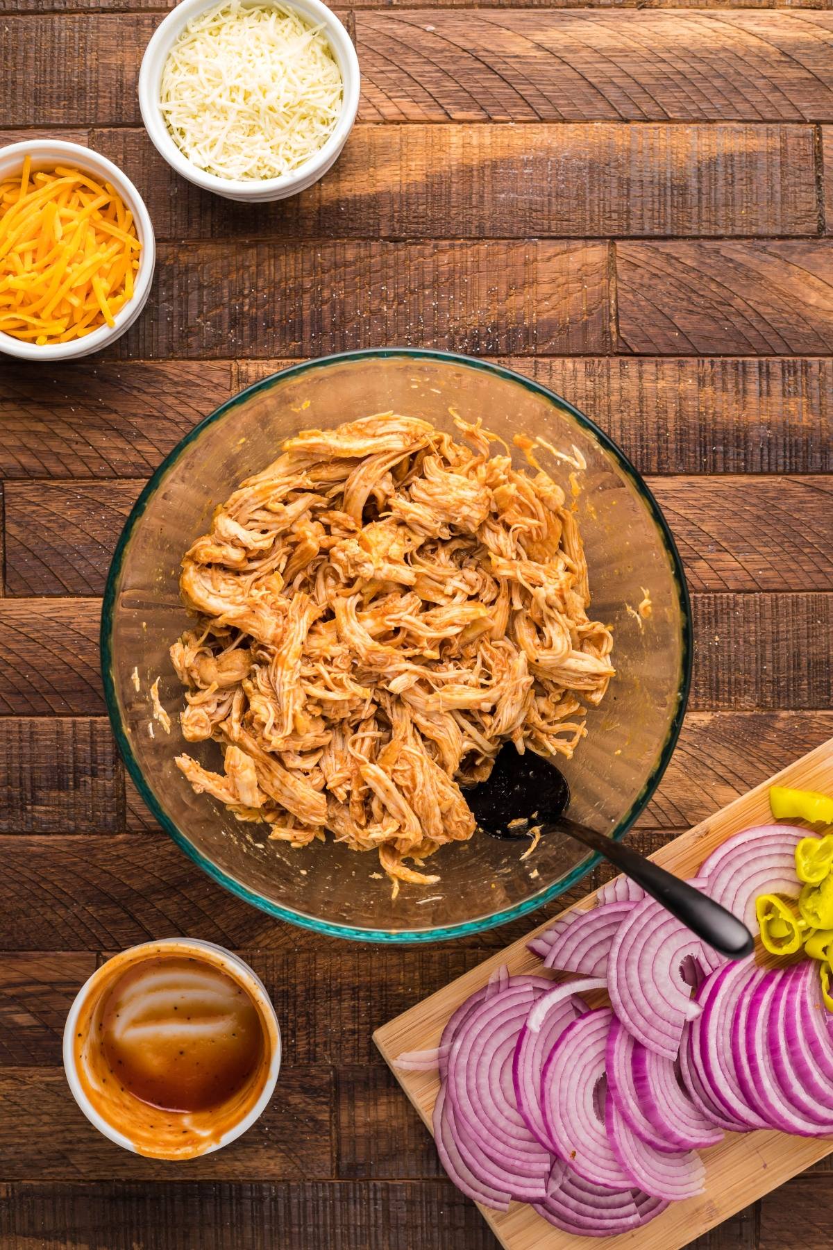 A bowl of shredded BBQ chicken with sliced red onions, cheese, sauce, and peppers on a wooden table—an easy chicken pizza-inspired 20 minute meal bursting with flavor.