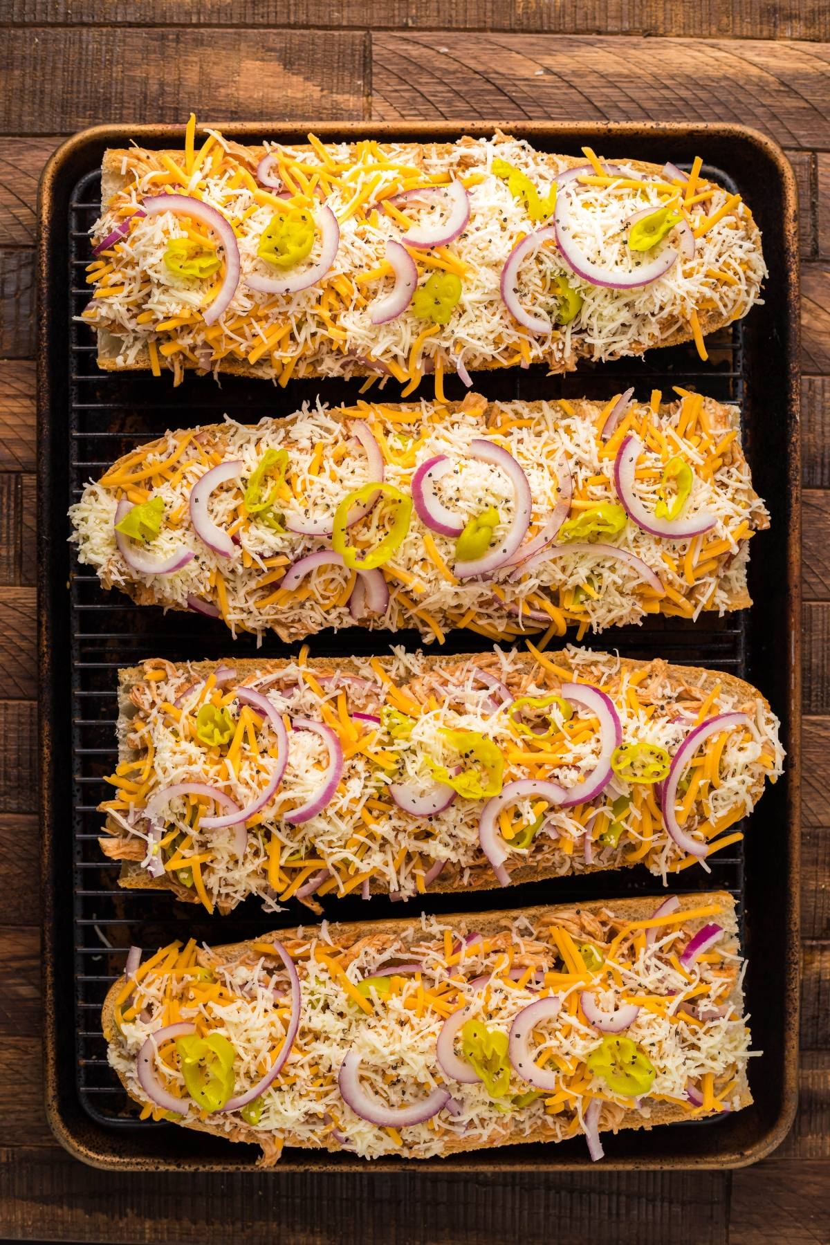 Four French bread halves topped with shredded cheese, red onion slices, and pepper rings on a baking sheet—perfect for an easy chicken pizza or a flavourful Instant Pot BBQ Chicken French Bread Pizza night.