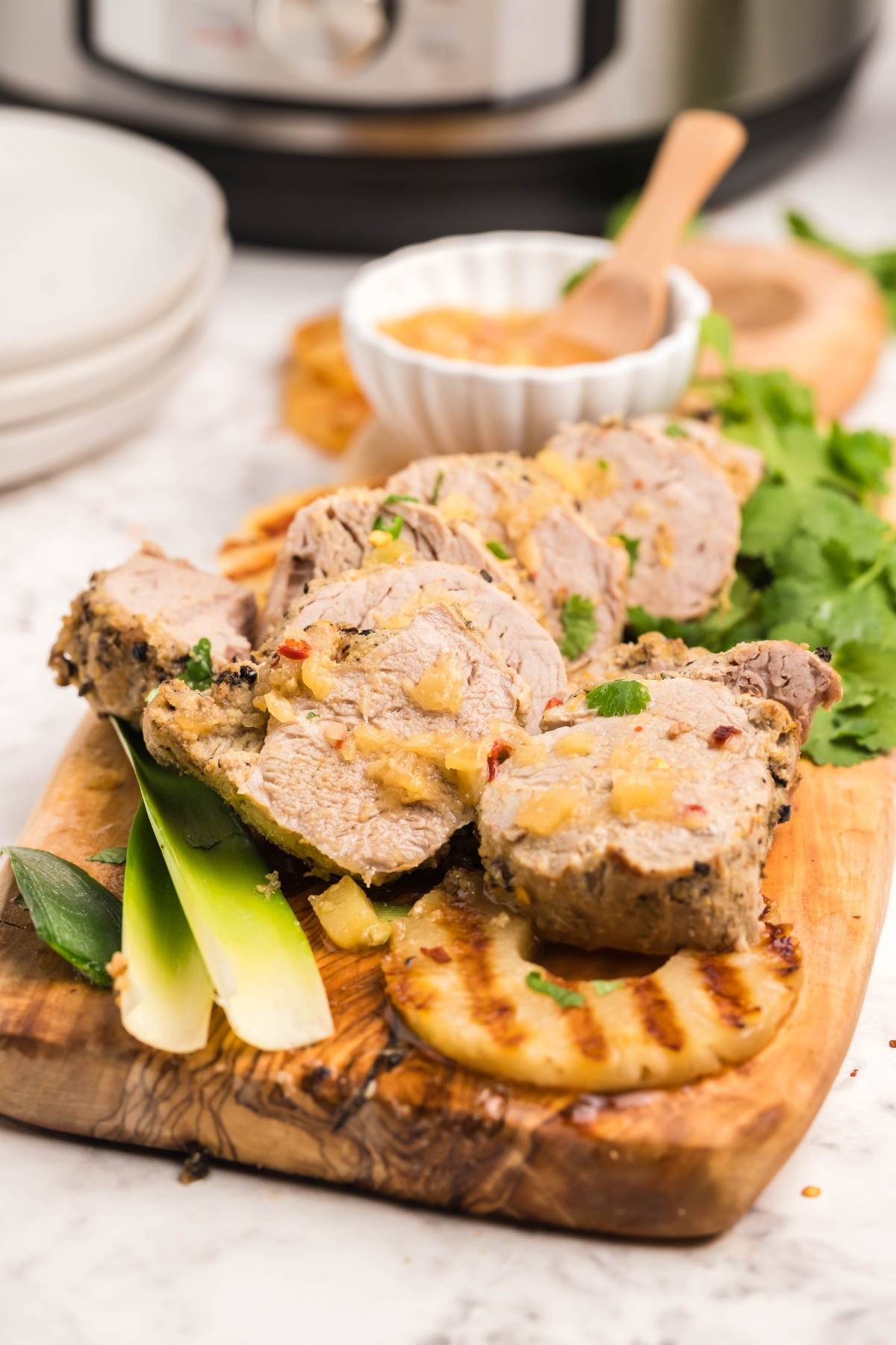 Sliced pork tenderloin with sauce on a wooden board, garnished with herbs and grilled flatbread—a Hawaiian inspired recipe for a flavorful twist.