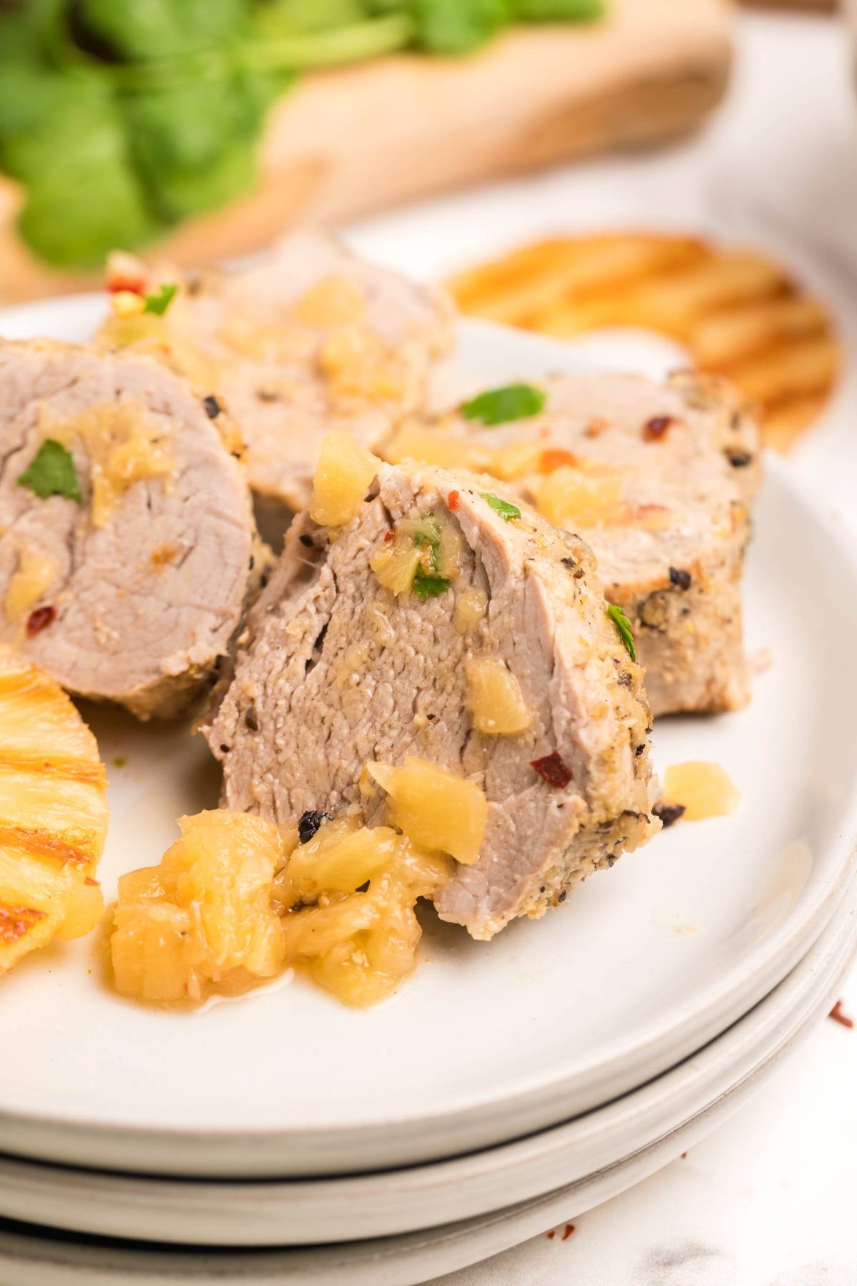 Sliced Instant Pot Hawaiian pork tenderloin with pineapple chunks, served on a white plate with grilled pineapple slices.