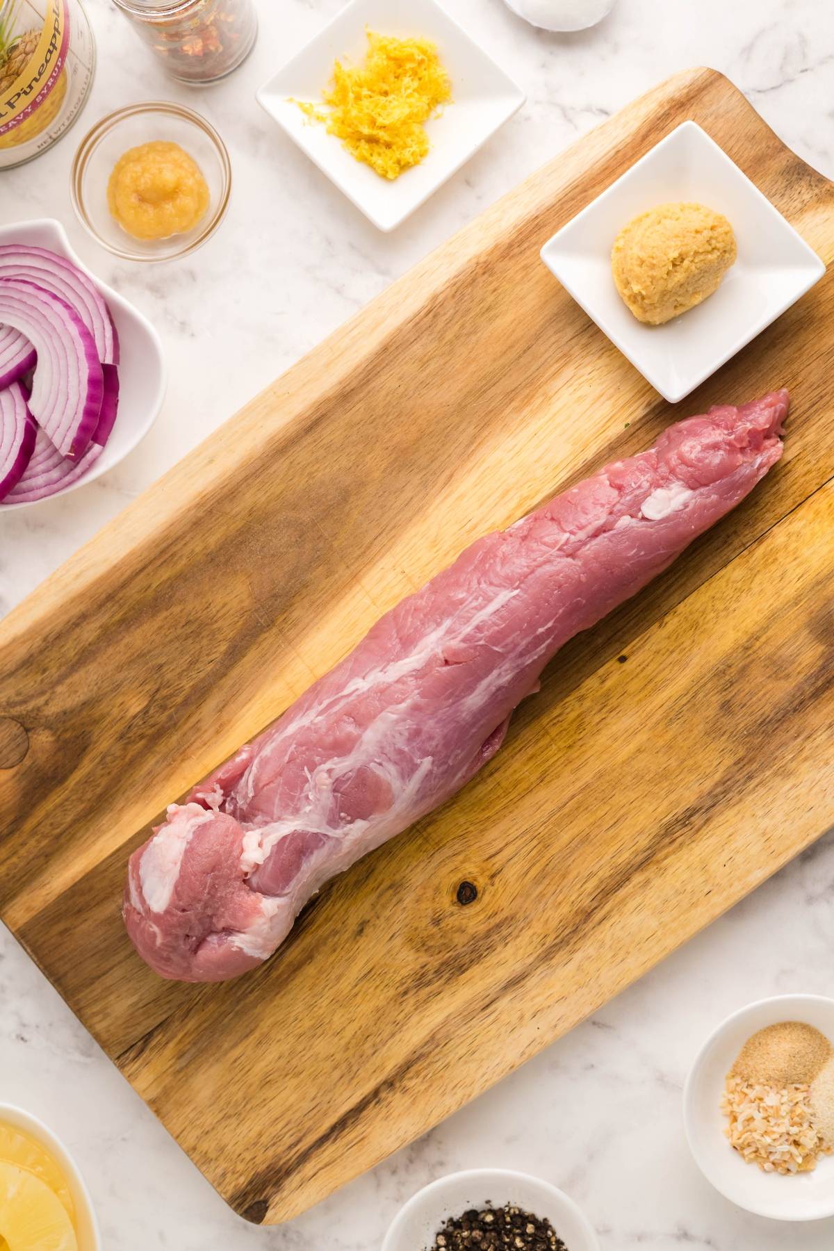Raw pork tenderloin on a wooden cutting board, surrounded by various seasonings and ingredients in small dishes—perfect for an easy Instant Pot pork tenderloin or Hawaiian inspired recipe.