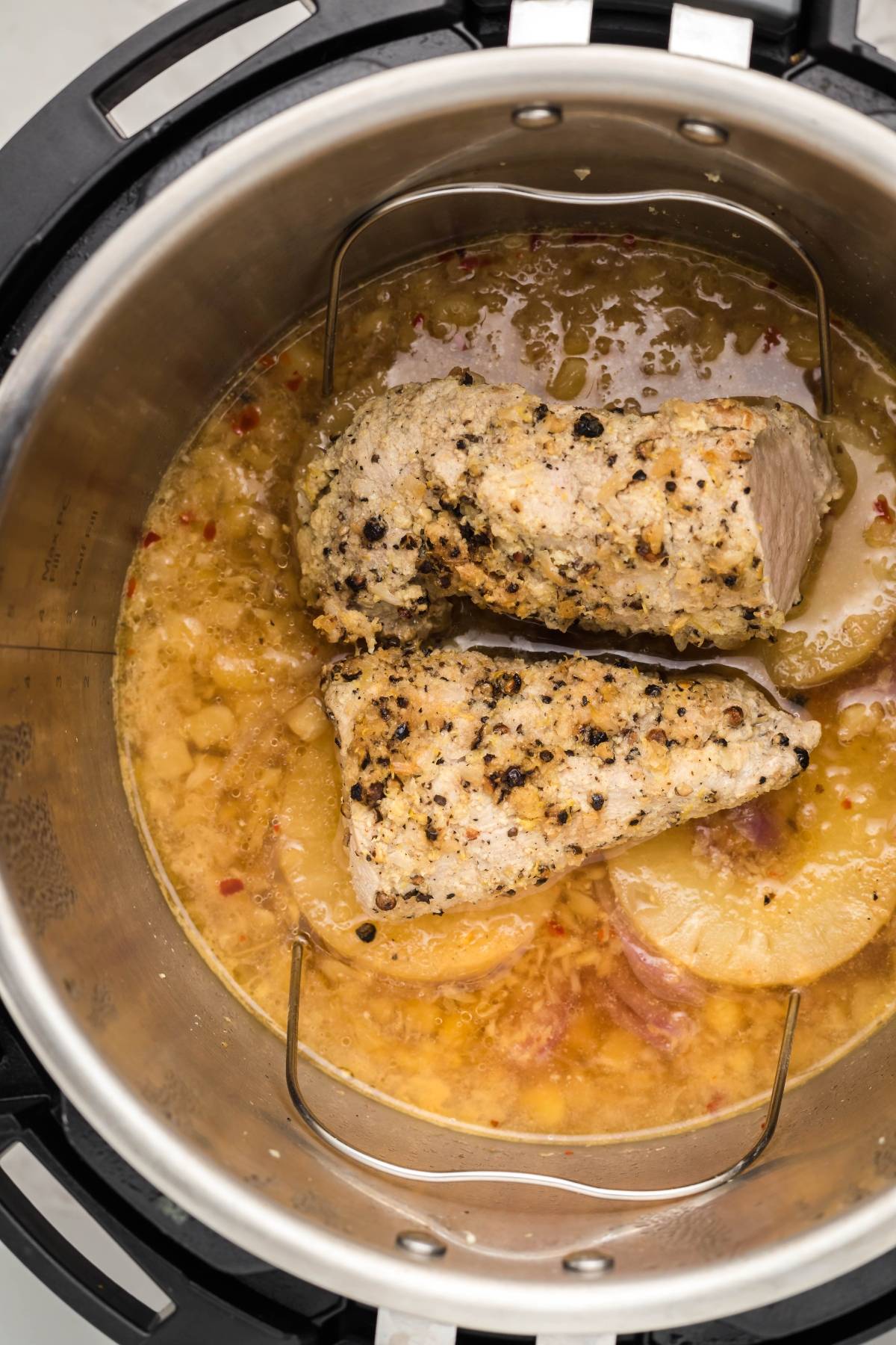 Two seasoned pork tenderloins cook in an Instant Pot with sliced potatoes and sauce for an easy instant pot dinner recipe.