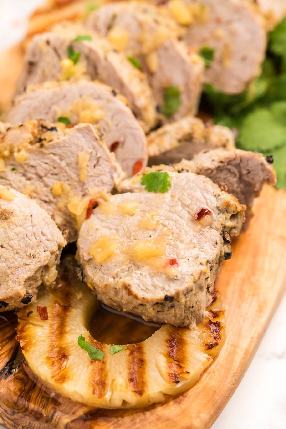 Sliced Instant Pot Hawaiian pork tenderloin served on a wooden board with grilled pineapple and fresh herbs.