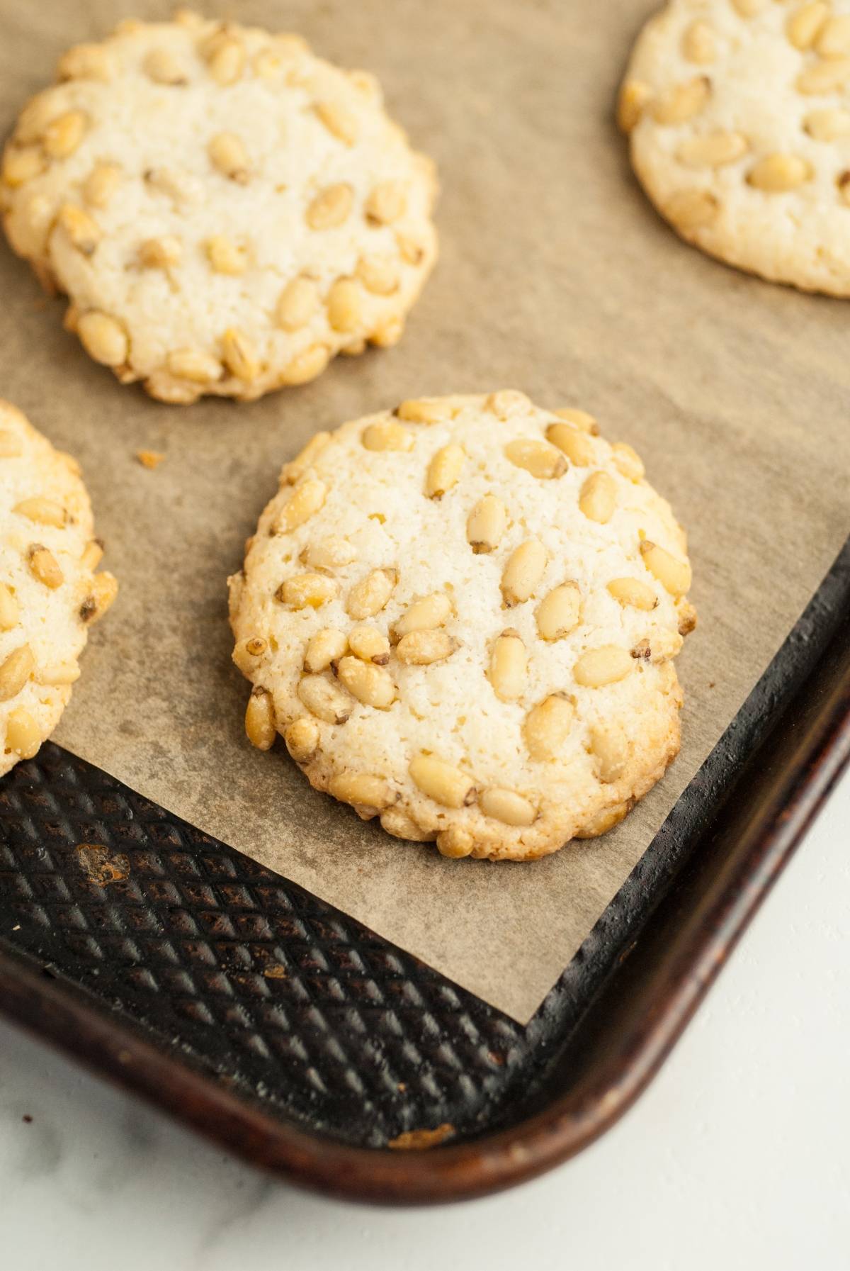 Round Italian Pignoli Cookies, known as one of the best Italian Christmas cookies, rest on a baking sheet lined with parchment paper.