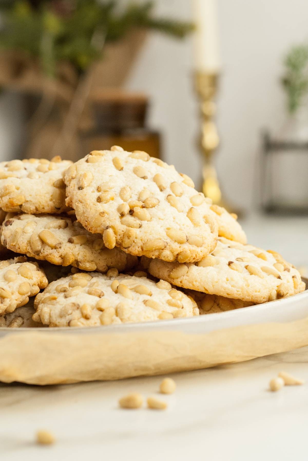 A plate of almond and pine nut cookies stacked on parchment paper, with some pine nuts scattered around—perfect for easy gluten free holiday baking.
