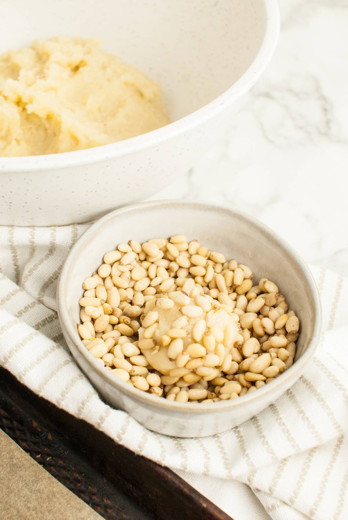A dough ball coated with pine nuts sits in a bowl beside a larger bowl of unshaped dough, ready to become the best Italian Christmas cookies with this easy pignoli cookie recipe.