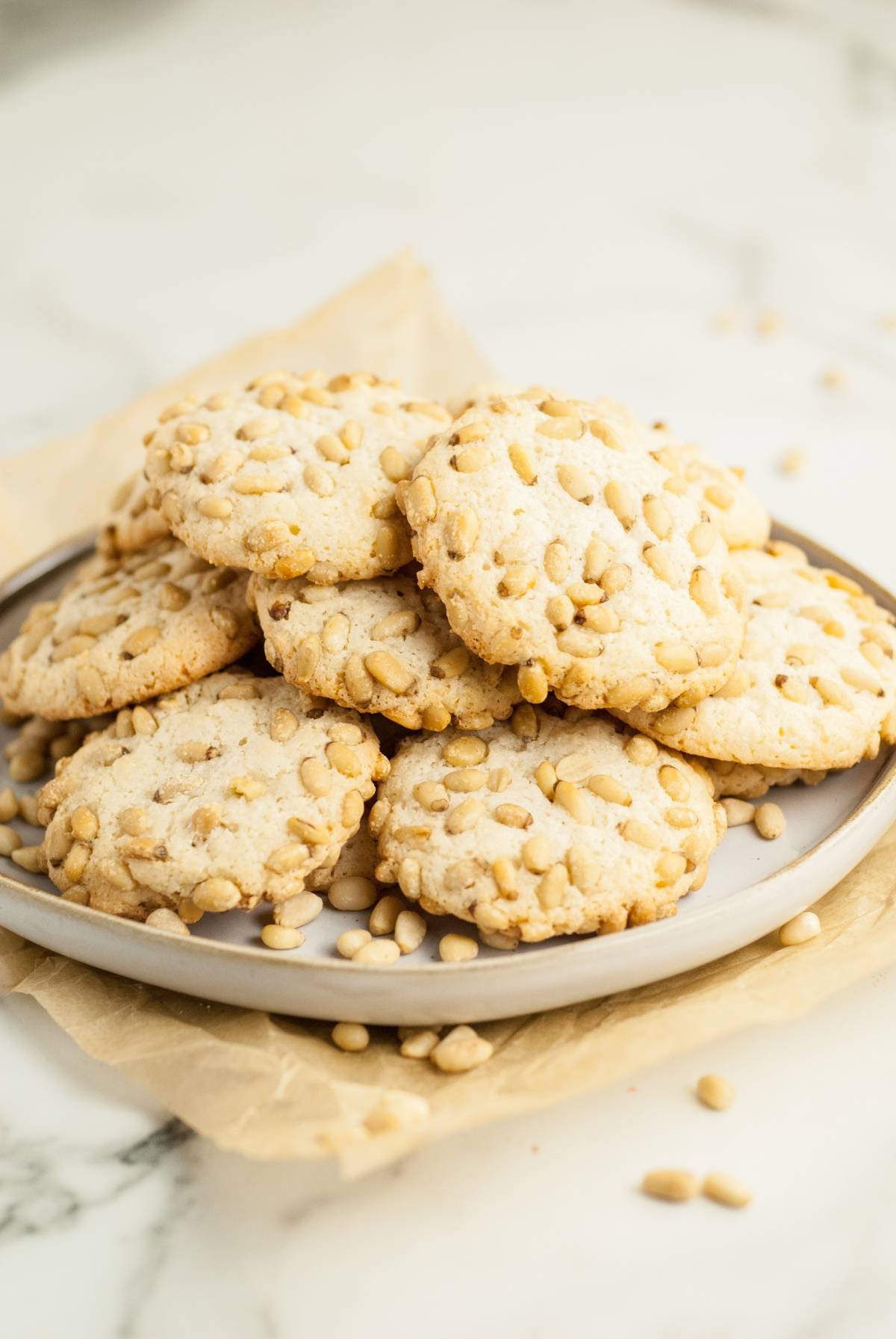 A plate of Italian Pignoli Cookies—almond and pine nut cookies—stacked on parchment paper atop a marble surface. Perfect for easy gluten free holiday baking.