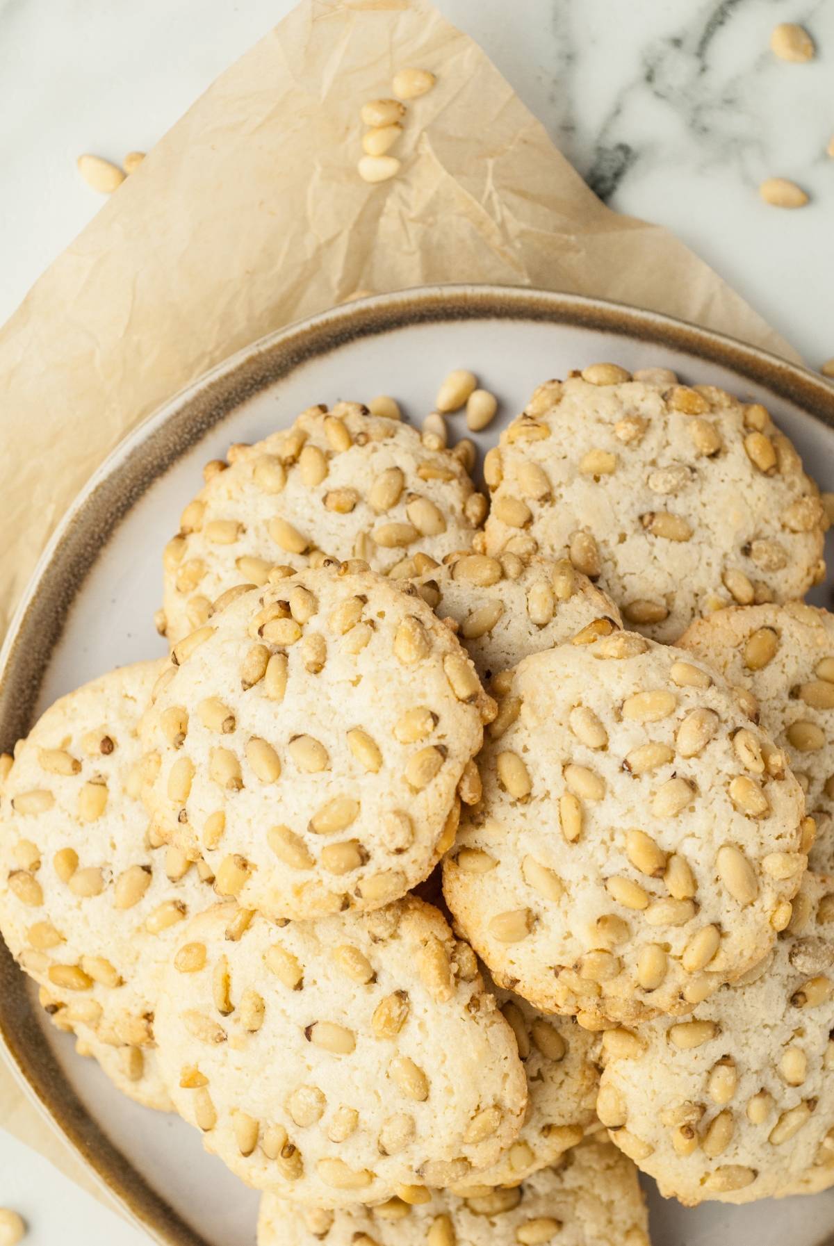 A plate of round almond and pine nut cookies, made with an easy gluten free holiday baking recipe, arranged on parchment paper on a marble surface.