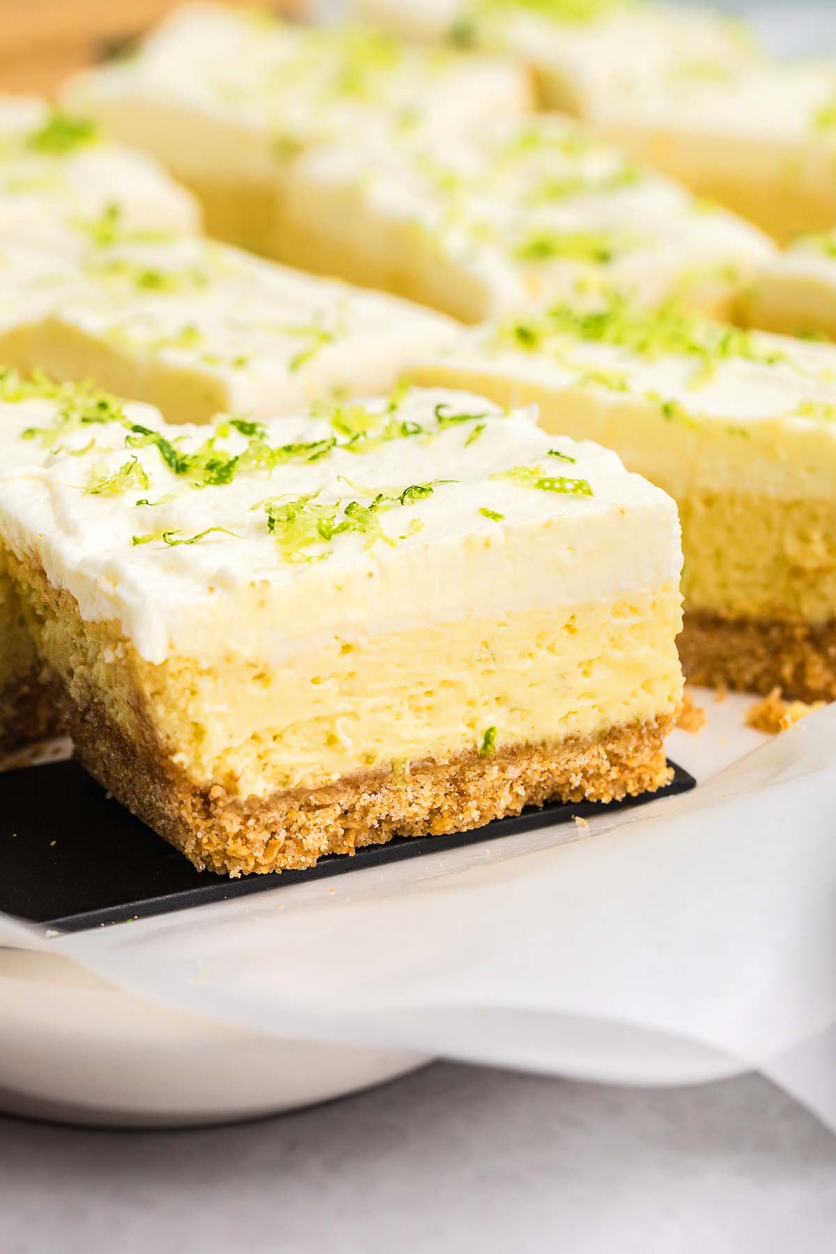 A close-up of creamy key lime bars with a graham cracker crust, topped with fresh lime zest.