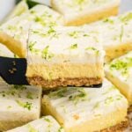 A spatula lifts a creamy, lime-topped key lime bar from a tray of similar dessert bars.