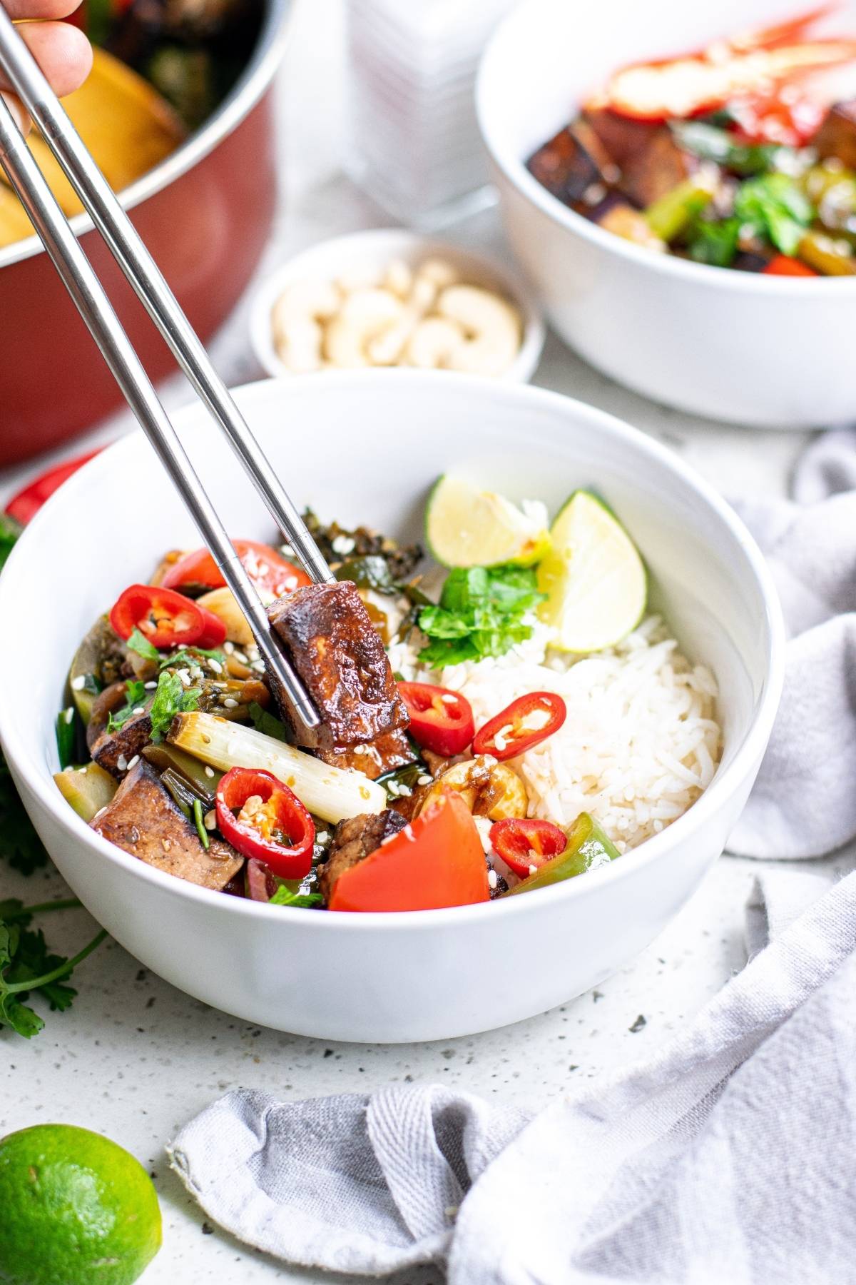 A bowl of rice and vegetables with tofu, topped with red chili, being picked up with chopsticks—a perfect Vegan Kung Pao dinner recipe.