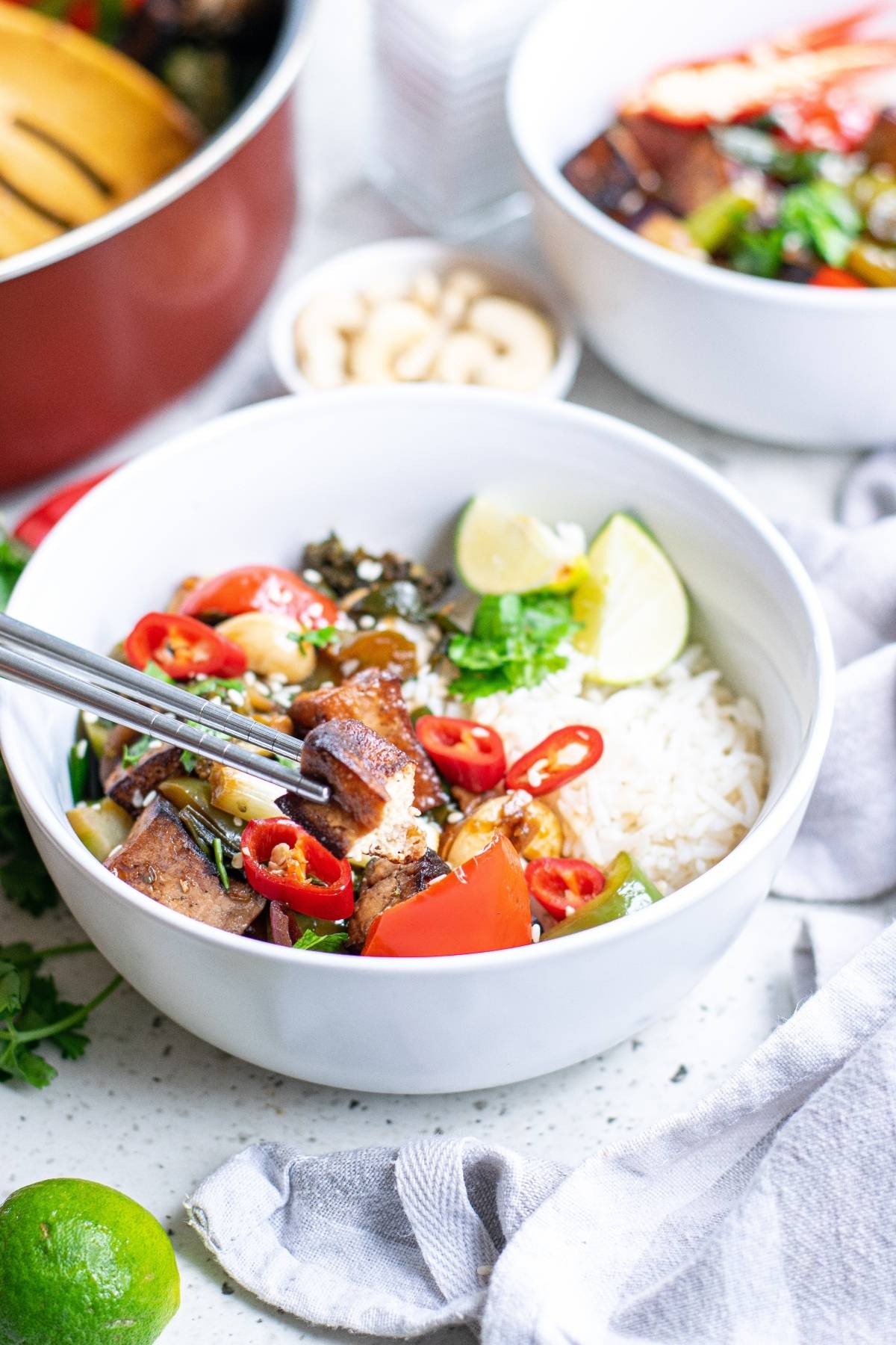 A bowl of rice with tofu, vegetables, red chili, and lime wedges, with chopsticks resting inside—a flavorful Vegetarian Chinese inspired dinner.