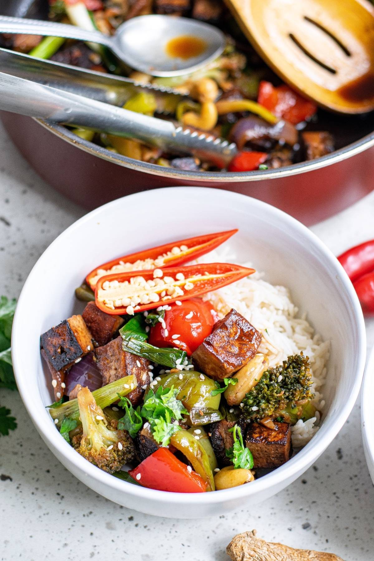 A bowl of rice with colorful stir-fried vegetables, tofu, and sliced red chili topped with sesame seeds—perfect as a vegan dinner recipe inspired by Kung Pao Tofu.